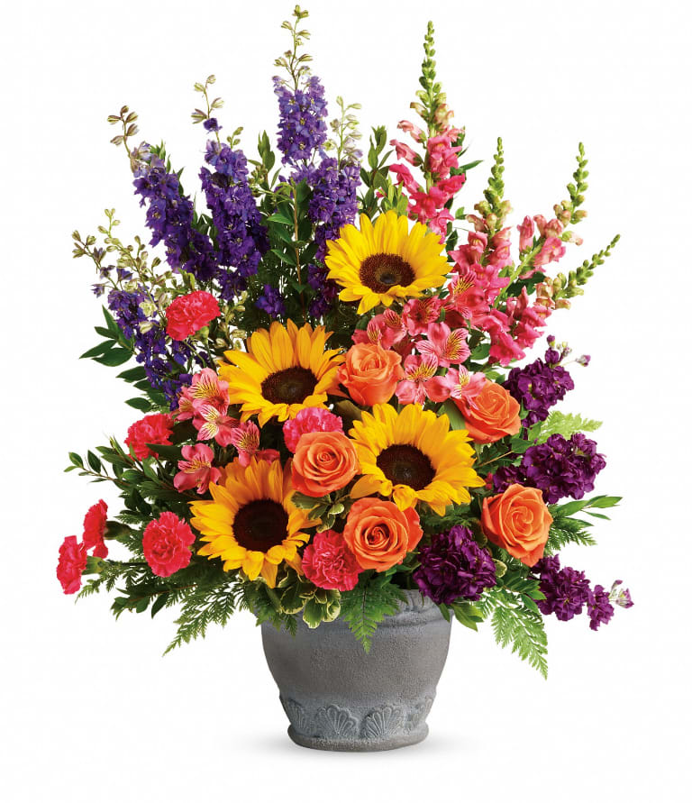 Hues Of Hope  - A colorful reminder that brighter days are ahead, this uplifting arrangement of sunflowers and roses in an elegant large antiqued pot brings joy and hope. This bright arrangement includes orange roses, pink alstroemeria, hot pink carnations, yellow sunflowers, purple larkspur, purple stock, hot pink snapdragons, myrtle, variegated pittosporum, and leatherleaf fern. Delivered in a Parisian Garden Pot. Approximately 23&quot; W x 30&quot; H