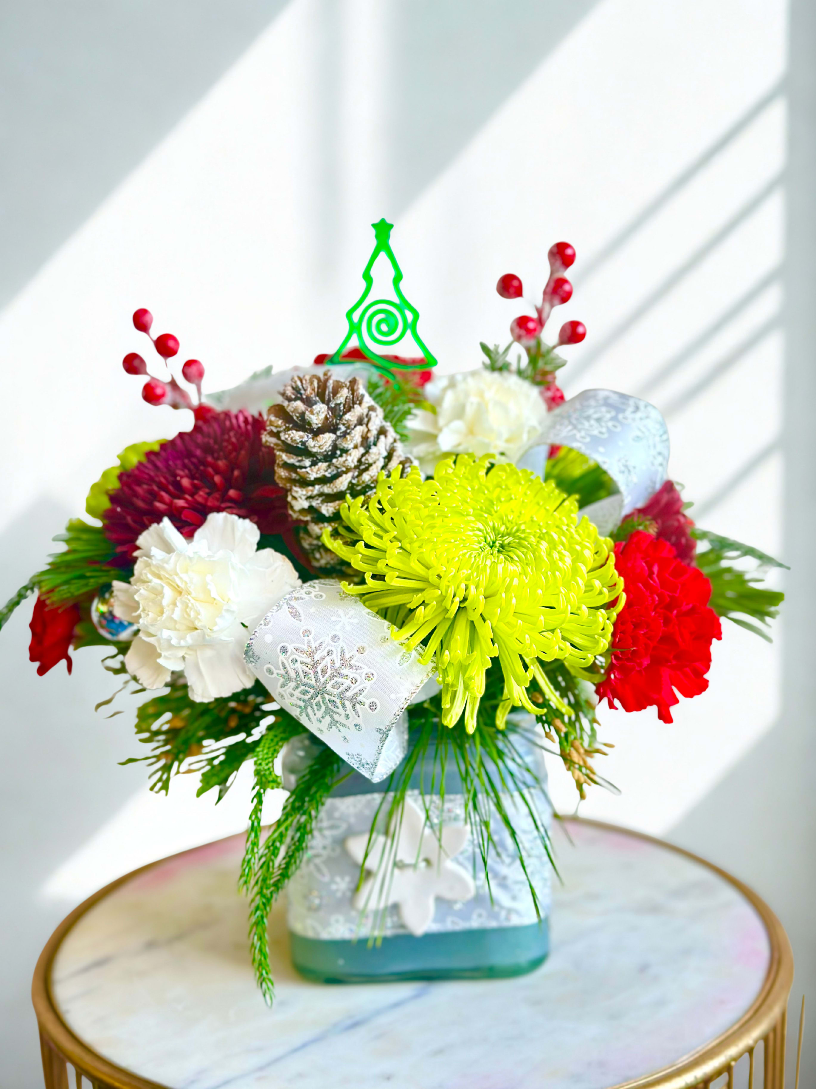 Happy holidays floral Arrangement - Happy holidays is a festive and luxurious floral arrangement that captures the magic of the holiday season. Lush red and white roses are artfully arranged with a cheerful Christmas mix of seasonal evergreens, shimmering ornaments, and vibrant red berries. Sprigs of classic holly berries and a decorative holiday ribbon add rich texture and charm, enhancing the design’s warm, celebratory feel. Presented in a chic white designer vase, this arrangement blends elegance and holiday spirit, making it a stunning centerpiece for winter gatherings or a heartfelt seasonal gift. 