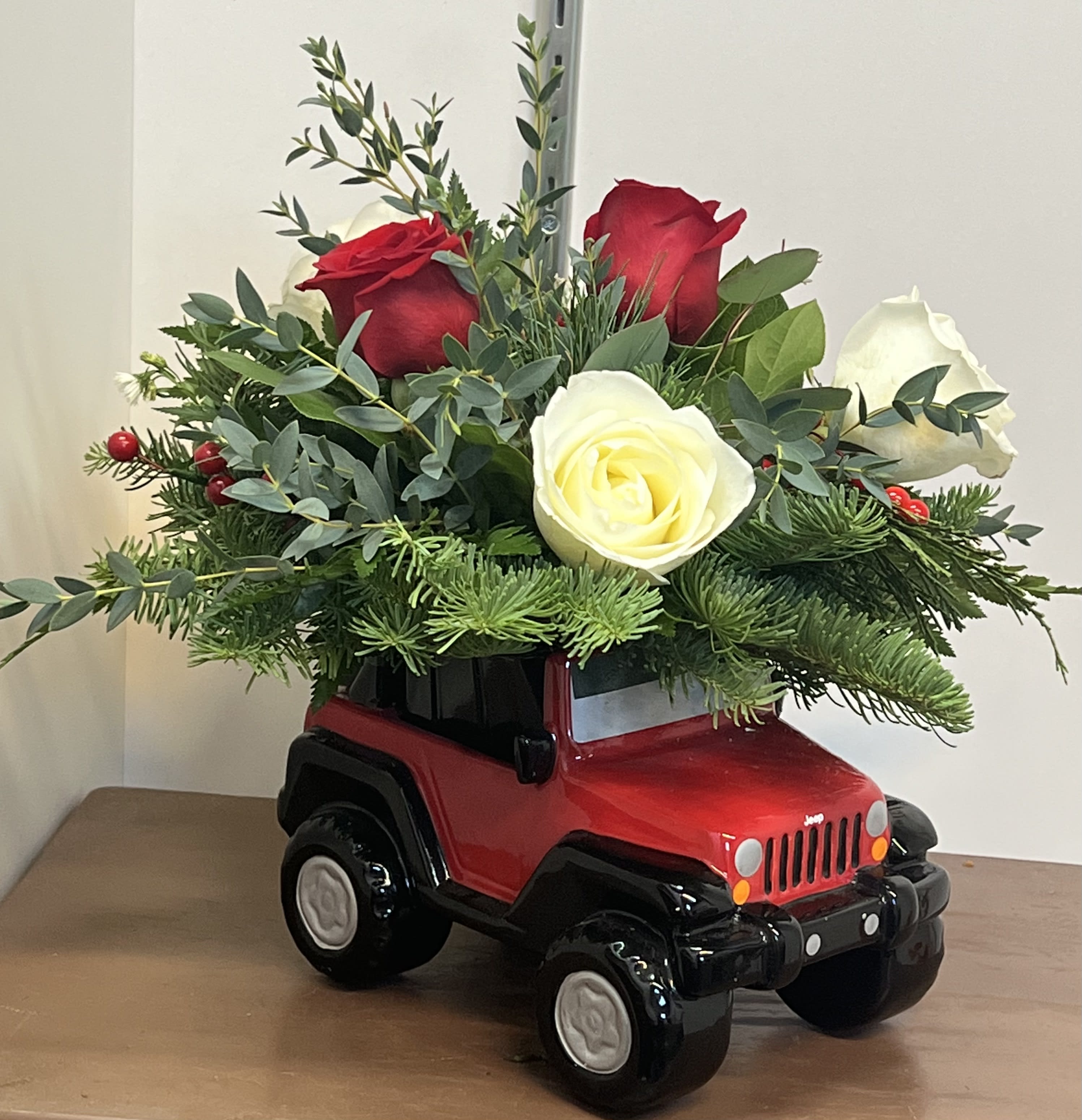 Jeep® Wrangler Winter Wheels Arrangement  - Enjoy this display of mixed winter greens and roses, designed in a collectible ceramic replica of the classic Jeep® Wrangler. This arrangement is customizable! Please leave design notes in the special instructions at checkout. 