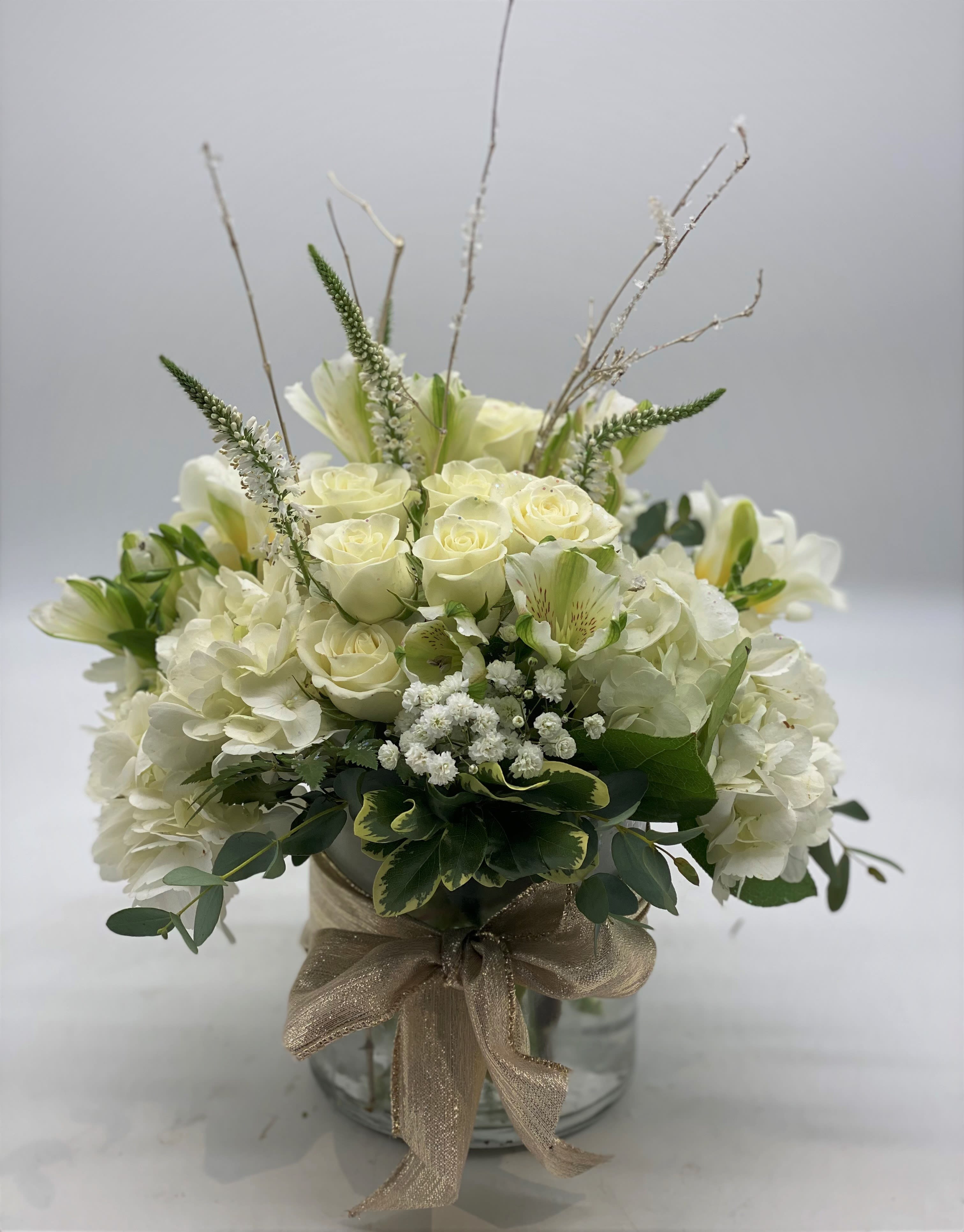 Glistening Snow - A lush mix of fresh white flowers arranged in a cylinder vase finished off with a beautiful gold bow, glistening winter sticks and shimmering glitter. Great for any winter occasion or just because!