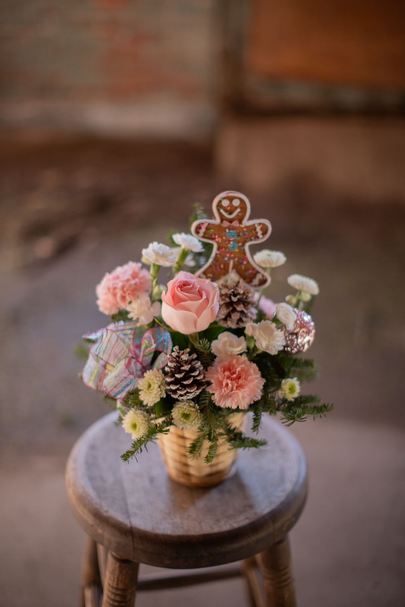 Freshly Baked in the Winter  - Do you enjoy baking or decorating? This sweet design is sure to thrill you without even turning on the oven. Nestled in an array of flowers is the sweetest gingerbread man you ever will see. Designed in a basket this arrangement includes roses, carnations, poms, ornaments, pine cones and a sparkly bow. 