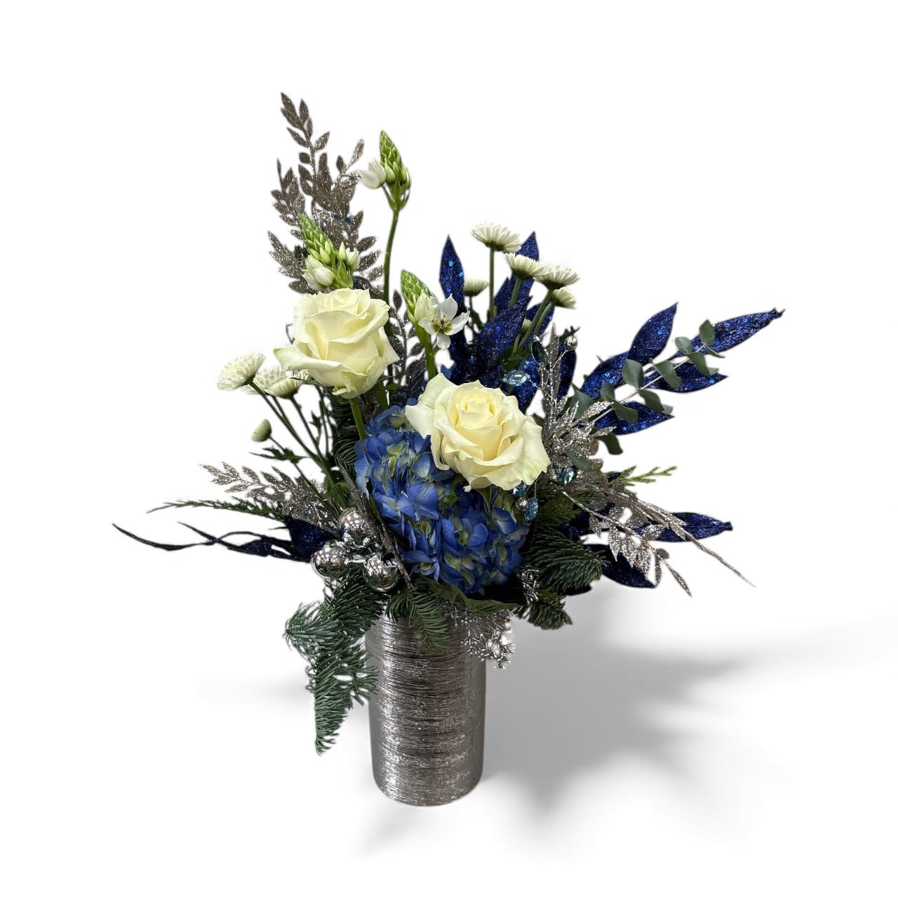 `Season of Light &amp; Peace  - Celebrate the season of lights with this festive blue and silver arrangement. Beautiful blue hydrangeas are paired with white rose, winter greens and other seasonal flowers. Accented with lots of sparked of blues and silvers all arranged in a silver ceramic vase. 