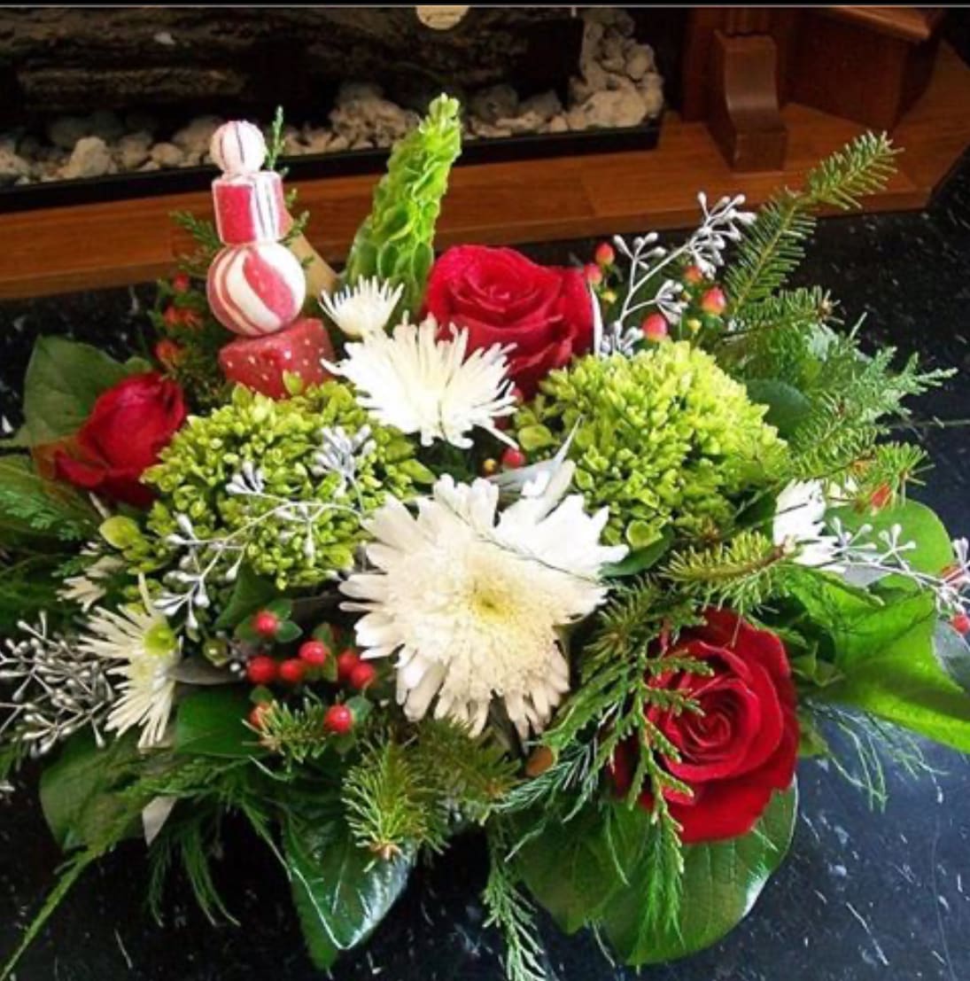 Candy Basket. A Floral Archist™ Original. - Basket design. A traditional color scheme of reds, whites and aromatic evergreens accentuated by silvers or golds organic elements, adorn with traditional mint candy. These festive arrangement is designed in a handle-less basket. Just the right combination for anyone in your ‘Nice’ list. As with ALL our designs, selection of blooms vary with each Upgrade.   A great way to cheer up that special guy!  NOTE: Our flowers and greens are a gift from nature. It’s shade and depth might vary, design, aesthetic and value remains the same. In support of our efforts to aide in the preservation of our planet, PJf uses Fair Trade flowers, Plants, Upcycled and Recycled containers. 