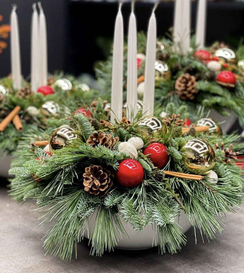 Designers Choice - Christmas Centerpiece - You choose the price point and our designer will create a festive centerpiece filled with candle(s)** pine, cedar, and/or spruce greens with embellishments such as bulbs, lotus pods, bows, pinecones and/or flowers. Bring a twinkle of light to your winter dinners.   **Candle for decorative purposes.  If you choose to light the candle do not leave burning unattended.  Keep wic trimmed to 1/4". Discard candle once it burns down to within 4" of greenery and flowers.