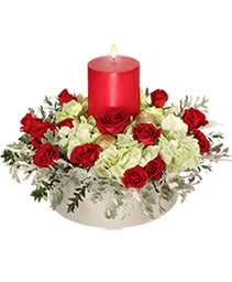 Holiday Motif Centerpiece - Christmas centerpiece with white hydrangea, red spray roses, filler flower and Christmas greens with a large hurricane candle in the center to top off the festive look for your table!