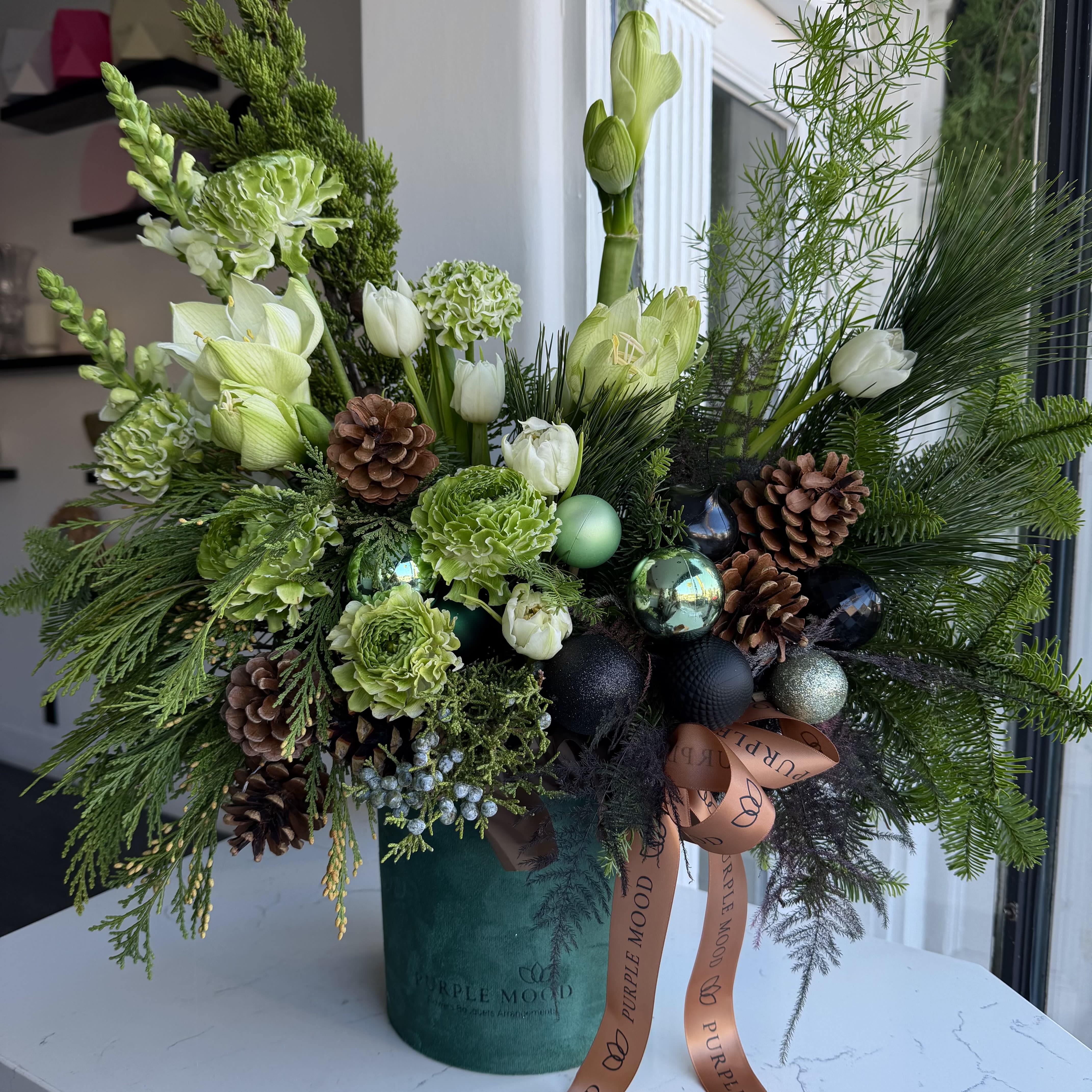 Pine Forest Box - Inspired by the stillness of a winter forest, this arrangement combines fresh evergreens, white tulips, pinecones, and metallic ornaments. A refined and nature-inspired holiday piece in a velvet vase.