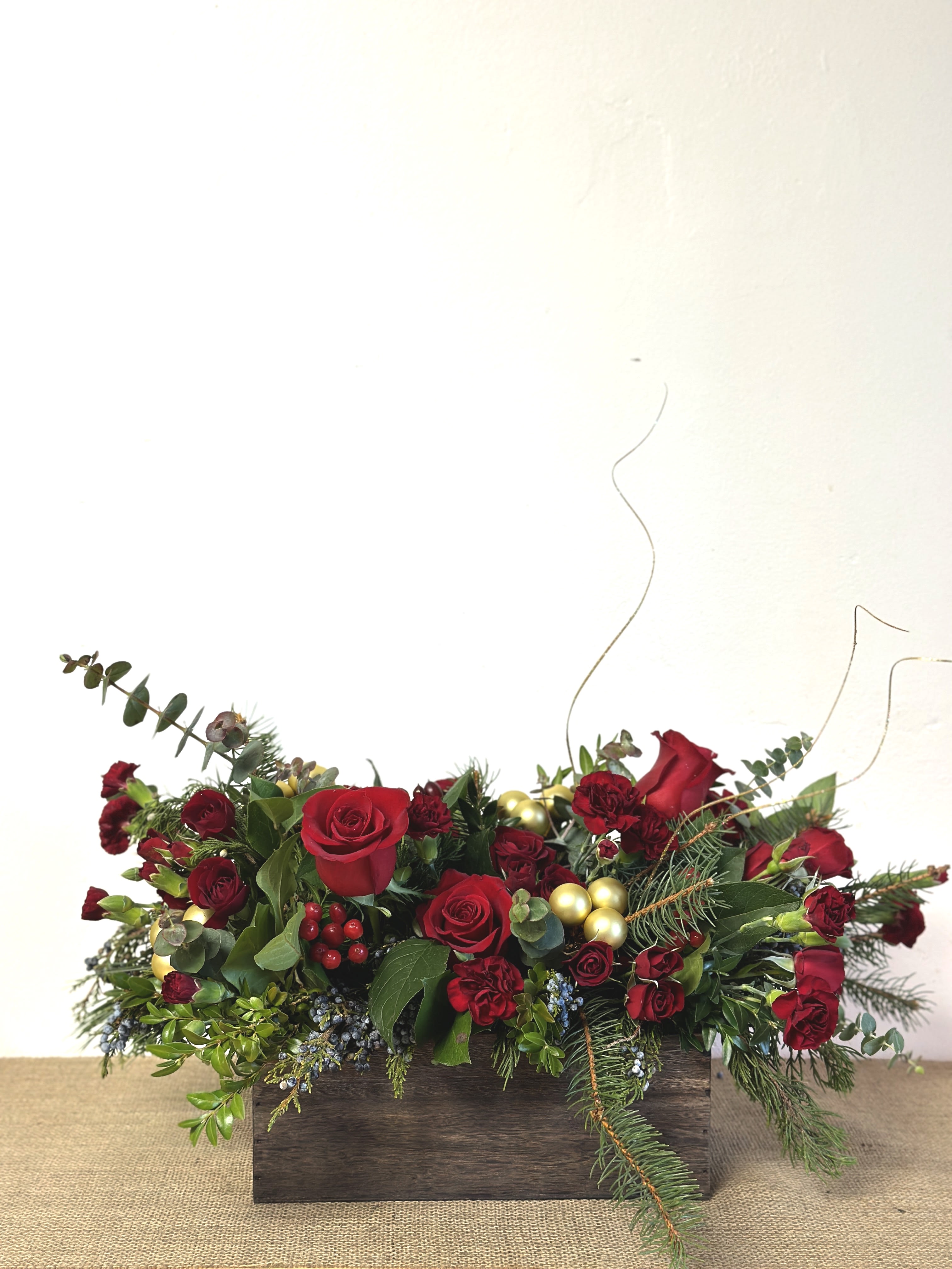Rustic Red - Fresh eucalyptus, roses, and winter greens in a subtle, rustic wooden container  