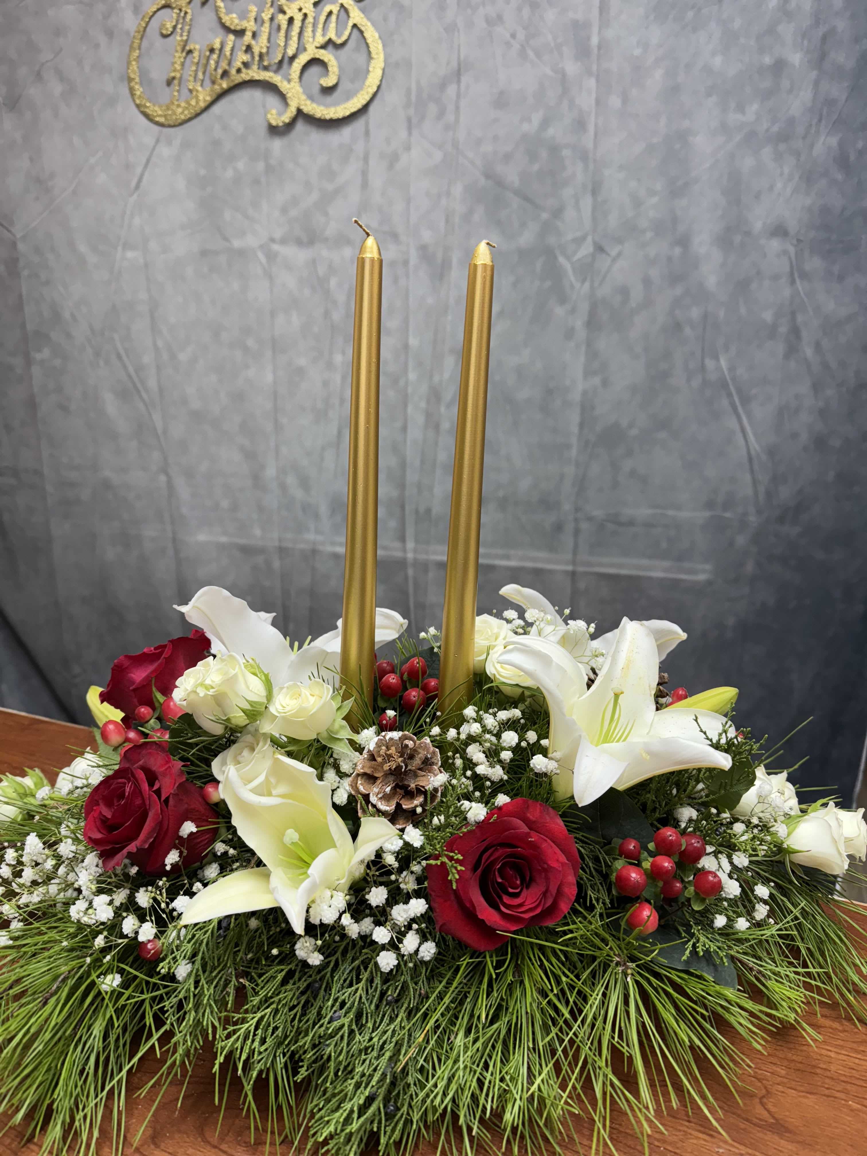 Evergreen Elegance - Celebrate the season with the timeless beauty of Evergreen Elegance Centerpiece .J&amp;S Floral introduces our newest Christmas-inspired designs, perfect for adding warmth and joy to your holiday celebrations  Elegant white lilies paired with red and white roses , vibrant red berries and pinecones , Christmas greenery and two red candles to brighten your holiday tablescape.  Each design is handcrafted with care to bring holiday cheer to your home or to gift someone special. Order now to make your Christmas unforgettable! Candles colors can vary depending on the availability (red, gold , white)