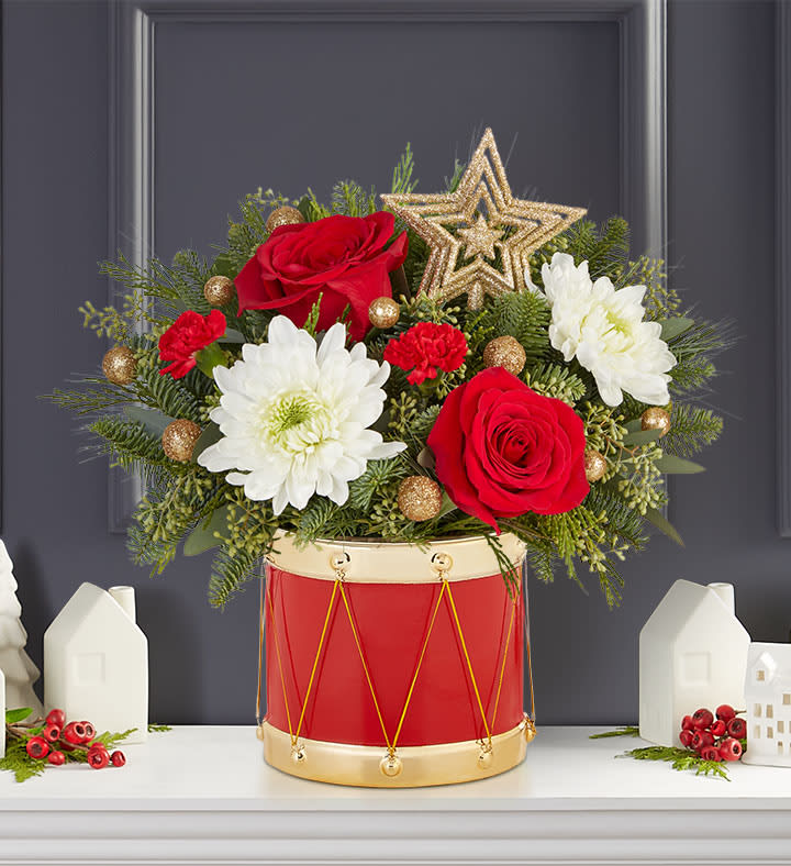 Musical Merriment™ Arrangement - The joy of gift-giving comes alive in our bright and festive arrangement. We’ve gathered red &amp; white blooms, Christmas greens, glittery gold ornaments and a gold star in our exclusive Musical Merriment drum container, inspired by the Nutcracker. Full of vintage charm, it’s a gift that delivers the magic of the season.  All-around arrangement with red roses and mini carnations; white mums; accented with seeded eucalyptus, assorted Christmas greenery Features gold glittered ornaments and five-point gold glittered star ornament keepsake topper Artistically designed in our exclusive Musical Merriment vintage-styled ceramic drum Our florists hand-design each arrangement, so colors and varieties may vary due to local availability