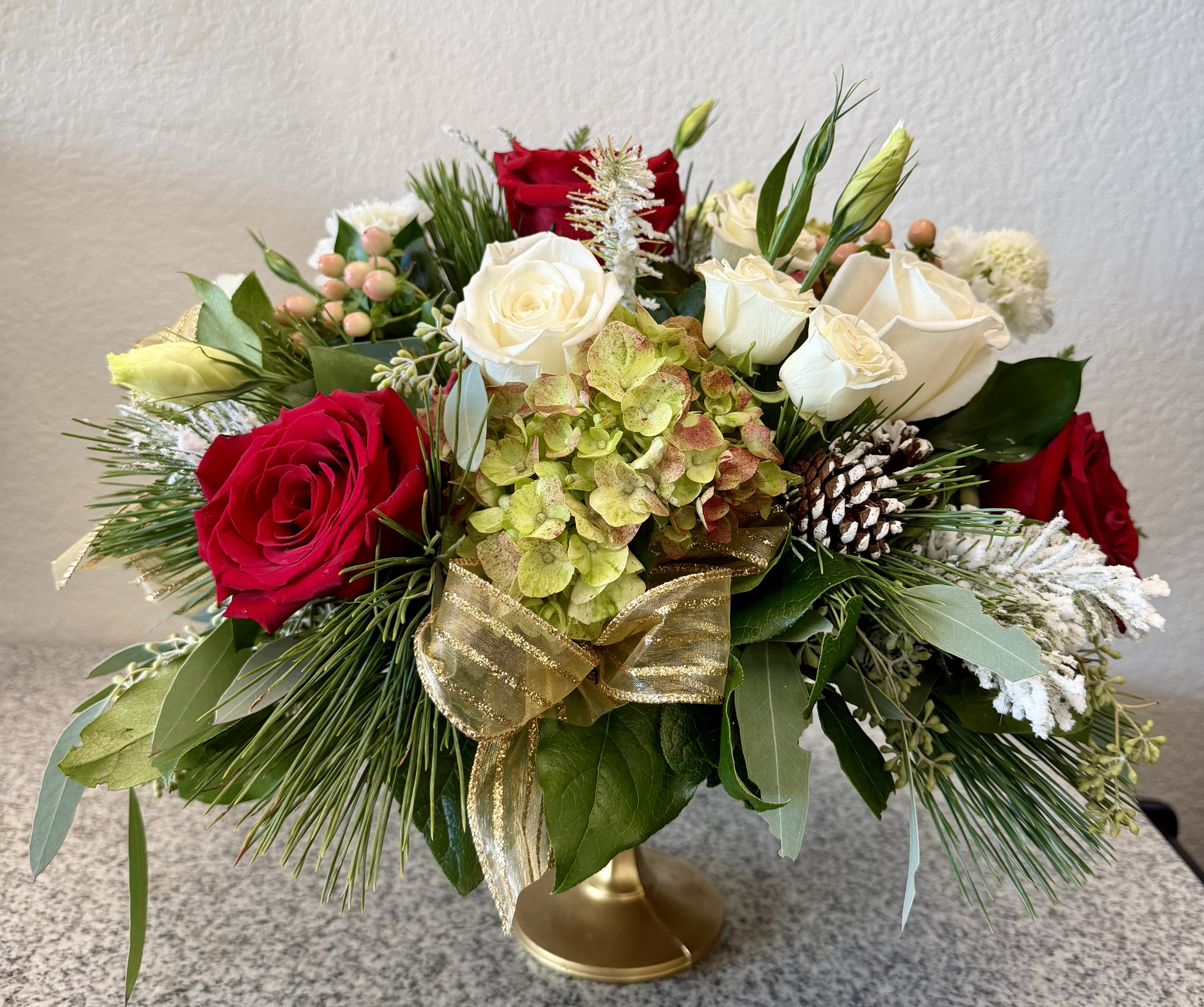 Christmas in Paris - red and white roses, spray roses, lisianthus, coffee bean, hydrangea and other flowers arranged in a gold urn vase with Christmas accents and greens