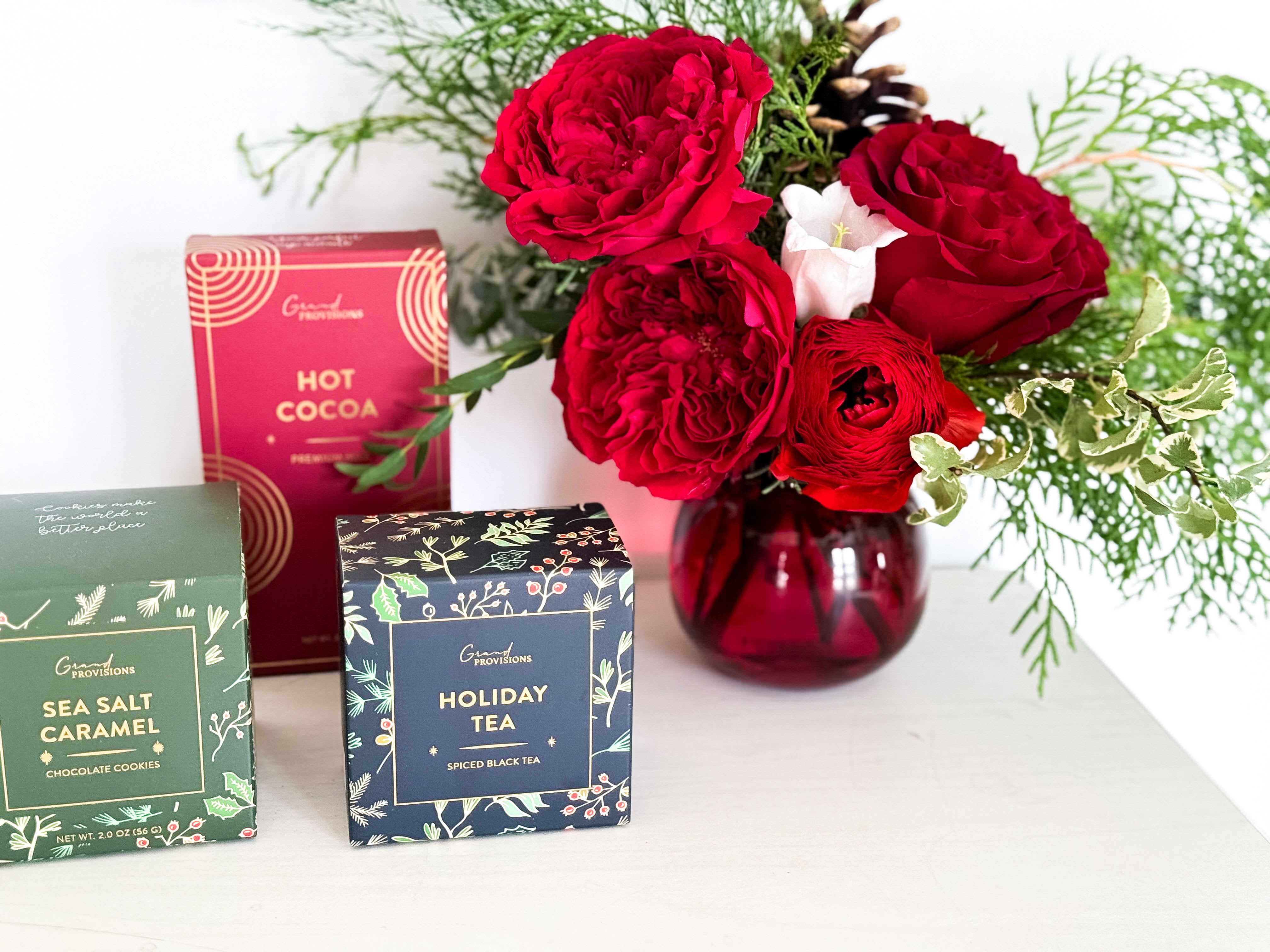 Winter Pick Me Up  - A small seasonal holiday arrangement designed in a red glass bubble vase, paired with Holiday Black Tea Blend, Holiday Hot Chocolate, and Holiday Sea Salt Caramel Cocoa Cookies