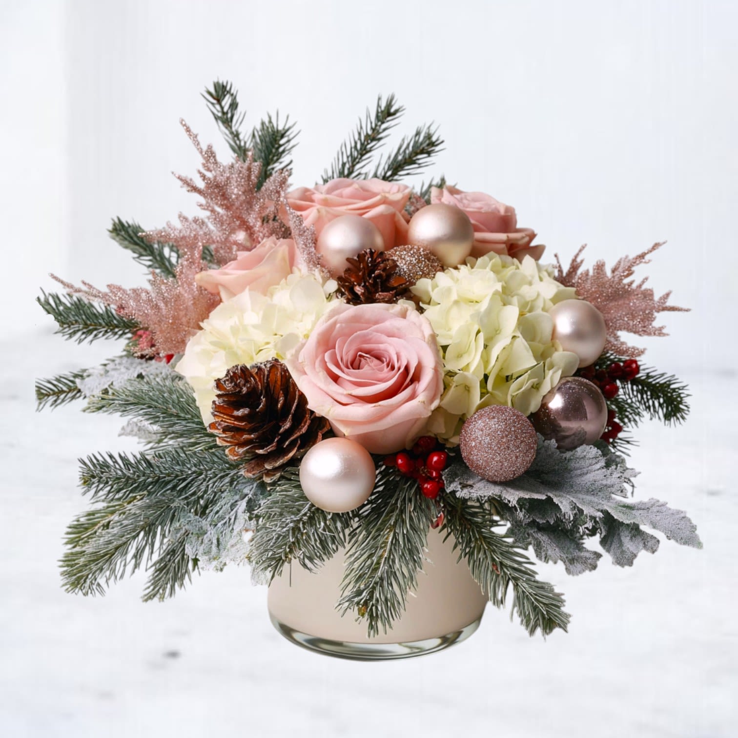 Blush Solstice - The Blush Solstice Arrangement blends soft blush tones with snow-kissed holiday textures for a romantic winter design. Featuring blush roses, ivory hydrangea, frosted evergreens, pinecones, red berries, and rose-gold ornaments, this arrangement brings a delicate, feminine warmth to the season. Arranged in a soft matte vase, it’s the perfect holiday accent for gift-giving, home décor, or winter celebrations.  Handcrafted by Whiskey Wallflower, each arrangement is designed to feel full, textural, and beautifully balanced for the holiday season.  Available for same-day delivery in Magnolia, The Woodlands, Conroe, Tomball, and nearby Houston communities.  Substitution Disclaimer: Seasonal flowers or accents may be replaced with premium alternatives of equal or greater value while maintaining the same palette and style.