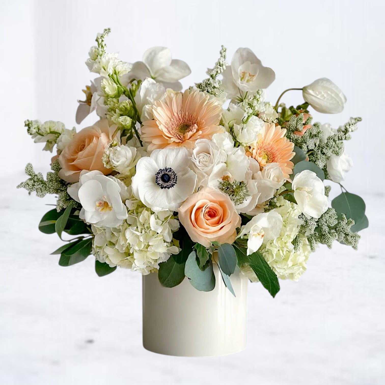 Dove Grace Bouquet - The Dove Grace Bouquet is a refined arrangement of soft peach roses, delicate white hydrangea, elegant orchids, and striking white anemones. Accented with blush gerberas and airy greenery, this bouquet exudes timeless sophistication. Presented in a modern white vase, it’s an ideal choice for anniversaries, weddings, sympathy gestures, or sending a graceful “just because” surprise. Available for same-day flower delivery in Houston and surrounding areas, the Dove Grace Bouquet is a beautiful way to share comfort, love, or celebration.