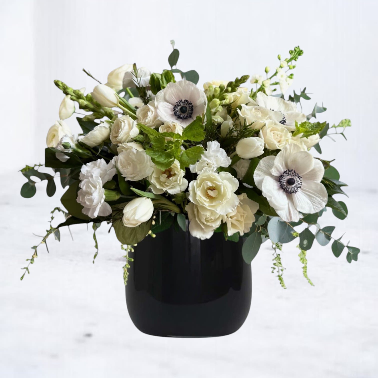 Moonlace - Moonlace is a poetic blend of light and shadow, featuring soft white blooms roses and striking white anemones with midnight centers nestled in a black vase, this arrangement evokes elegance with a modern edge. Perfect for sympathy gestures, anniversaries, or to elevate any space with timeless grace. Moonlace delivers a statement of quiet strength and refined beauty.  Available for same-day flower delivery in Houston, Magnolia, Montgomery, and surrounding areas.  If fresh anemones are unavailable, we may substitute with ranunculus. Both share a delicate, layered petal structure and bring the same soft, romantic charm to the arrangement. This substitution ensures the bouquet retains its beauty, texture, and premium quality while staying true to the original design. 