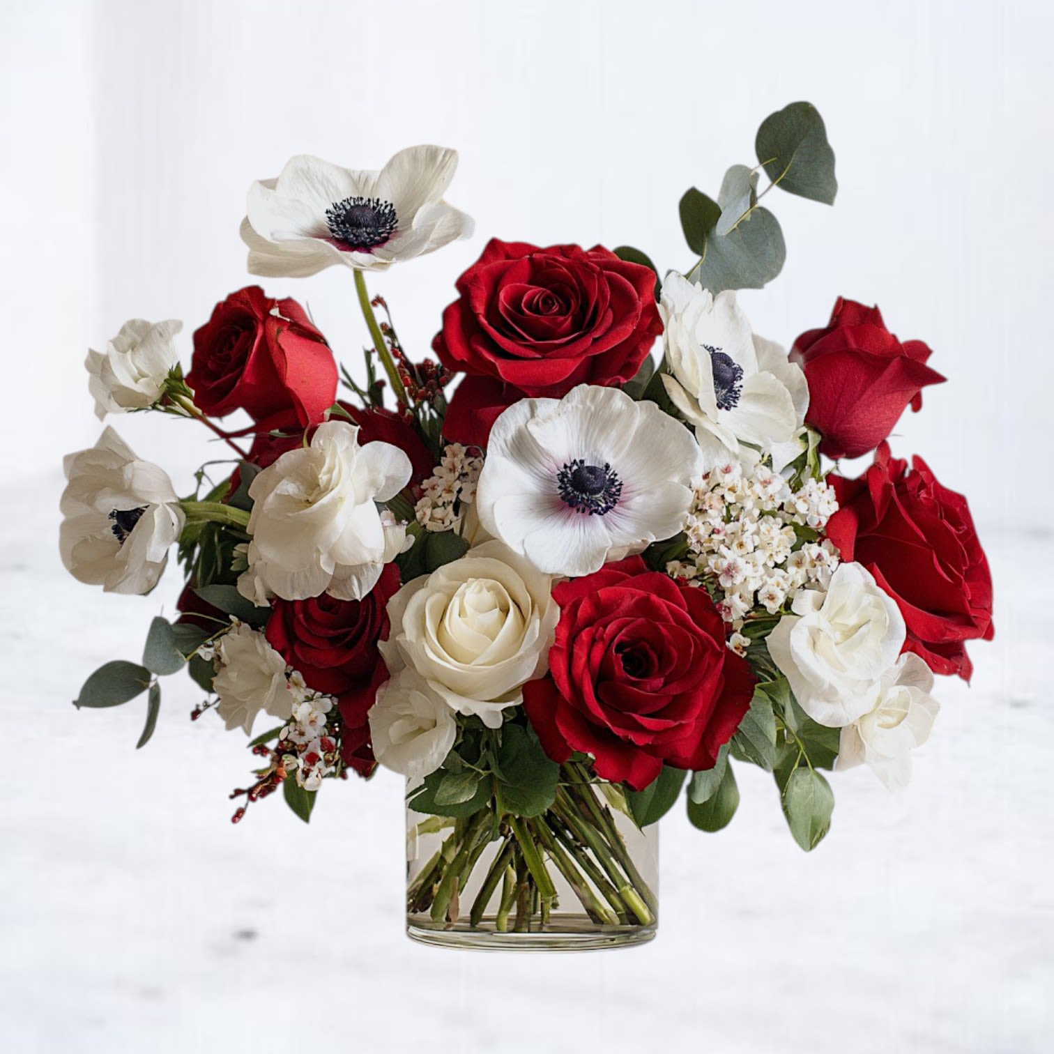 Eternal Devotion Bouquet - Celebrate timeless love with our Eternal Devotion Bouquet, an elegant blend of radiant red roses, crisp white roses, and striking white anemones accented with fresh greenery. This arrangement makes a breathtaking gift for anniversaries or simply to say “I love you.” Its bold red-and-white palette also lends itself beautifully to sympathy occasions, offering comfort and dignity with modern grace. Handcrafted in a clear glass vase, this bouquet is designed for lasting beauty and unforgettable impact.  Available for same-day flower delivery in Houston, Magnolia, The Woodlands, Spring, Conroe, and surrounding areas.