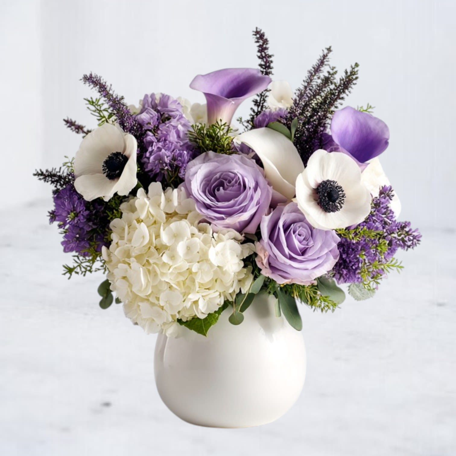Bluebell Muse - A graceful expression of remembrance, Bluebell Muse offers a soothing tribute for moments of farewell. This elegant floral arrangement features soft lavender and ivory blooms including calla lilies, roses, anemones, delphinium, and white hydrangeas, delicately arranged to evoke a feeling of peace and reflection. Cool-toned and thoughtfully designed, it serves as a gentle comfort during life’s most tender goodbyes. Perfect for funeral services, memorials, or sending condolences, Bluebell Muse is available for same-day sympathy flower delivery in Houston and surrounding areas.  *If fresh anemones are unavailable, we may substitute with ranunculus. Both share a delicate, layered petal structure and bring the same soft, romantic charm to the arrangement. This substitution ensures the bouquet retains its beauty, texture, and premium quality while staying true to the original design.