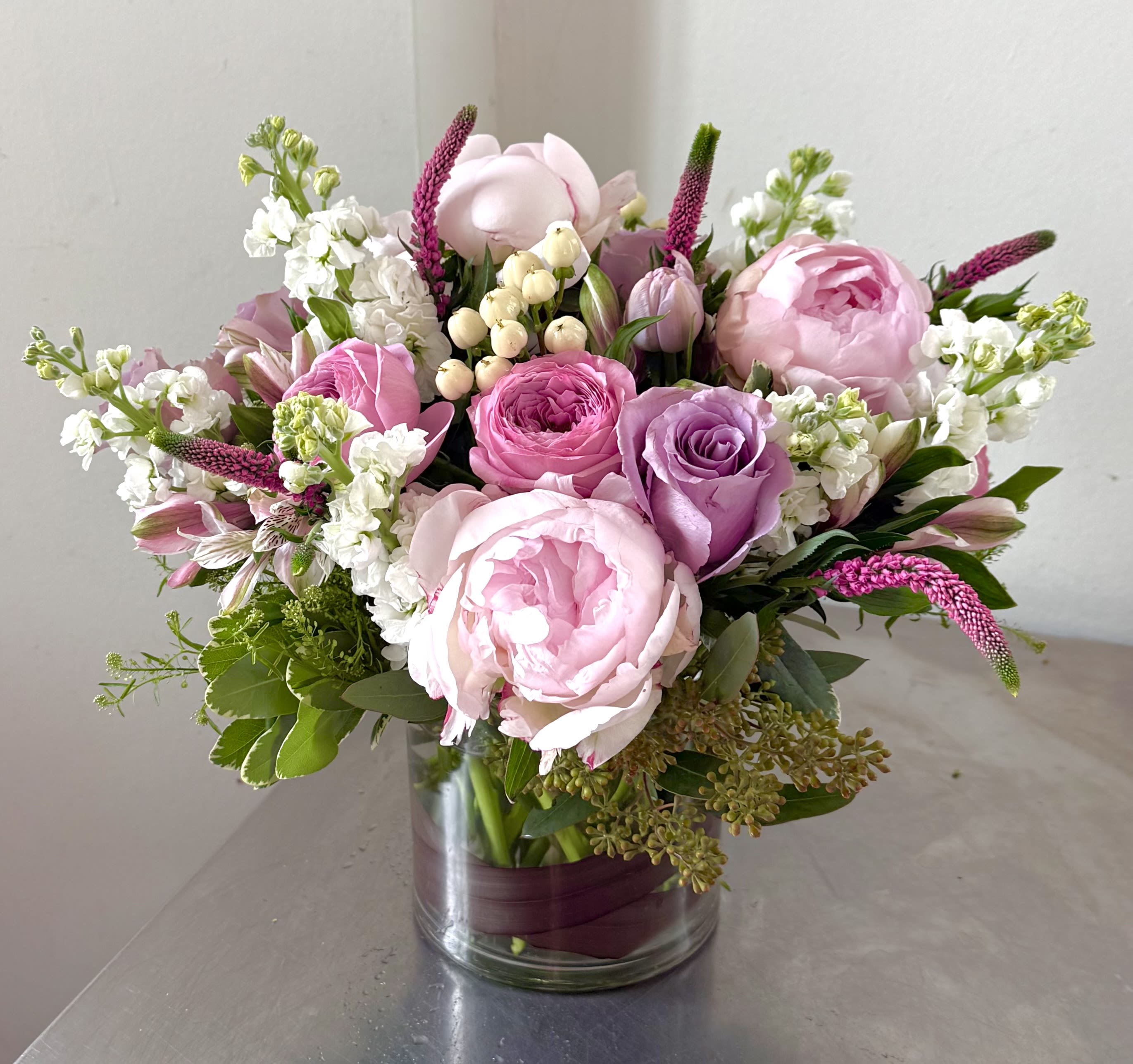 Blush Garden Luxe - Blush Garden Luxe is a lush, hand-crafted arrangement designed to celebrate elegance in every petal. Soft pink peonies, lavender roses, garden roses, white stock, alstroemeria, and accent blooms come together in a romantic color palette of blush, lilac, and cream. Arranged in a modern glass vase, this bouquet brings a fresh, airy glow to birthdays, anniversaries, thank-you gifts, and everyday celebrations.