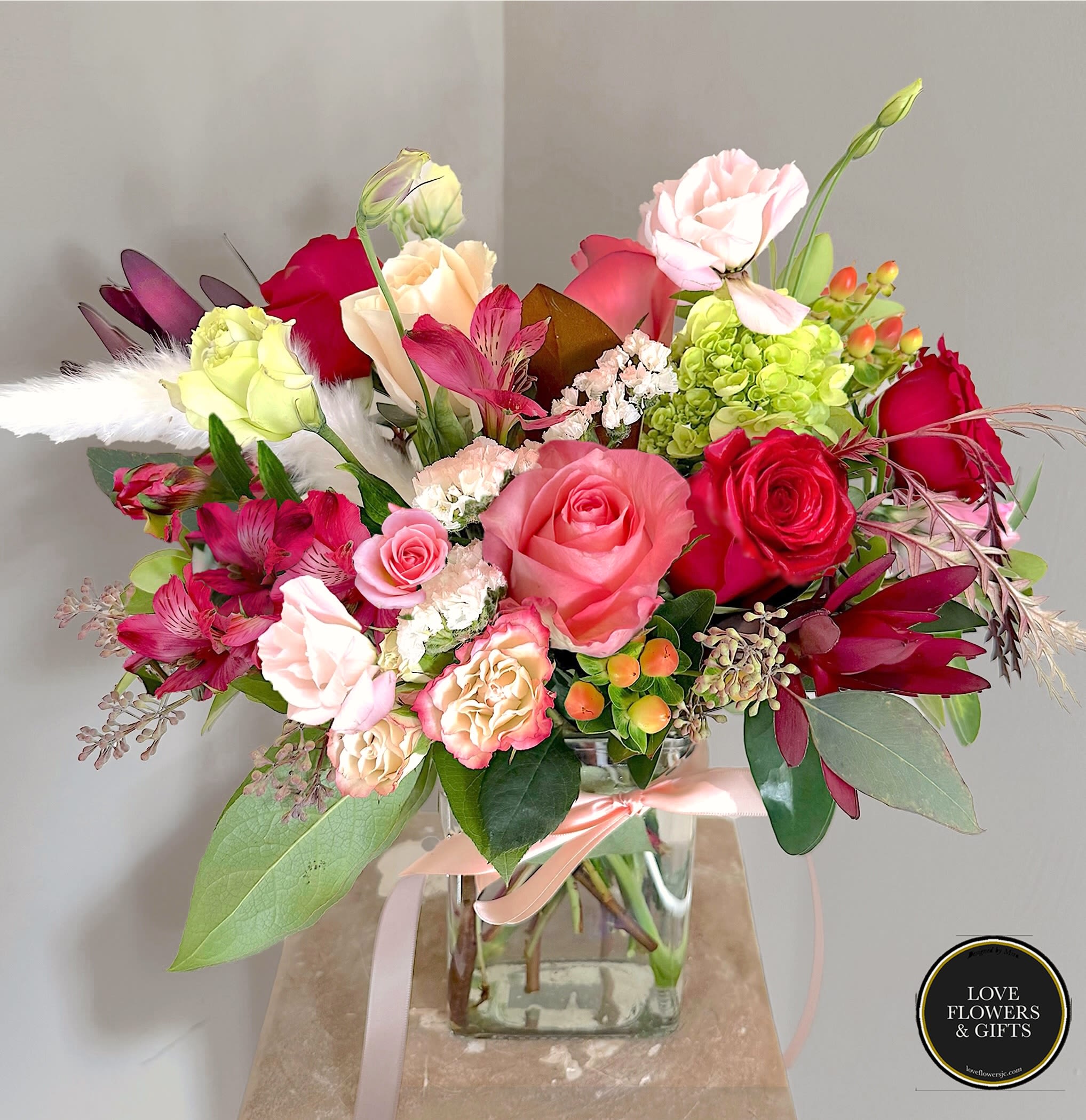 Mistletoe - Designed in a rectangular glass vase, made with corals, reds, and creams with a ivory ribbon. 