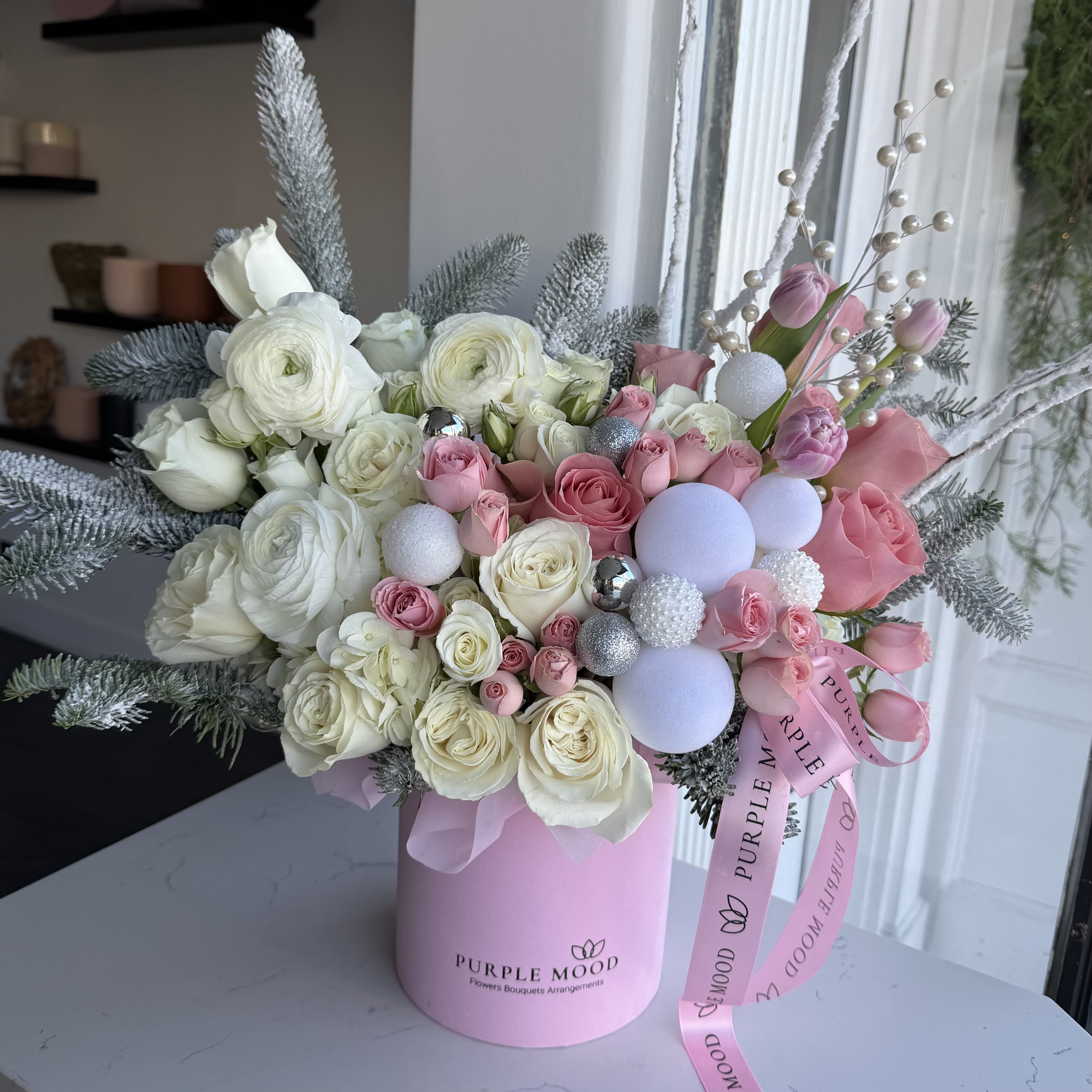 Cinderella Box -  Step into a fairytale with our enchanting Cinderella Box, a delicate blend of elegance and magic. This arrangement features blush pink roses, pristine white blooms, and exquisite orchids nestled amidst frosted greenery. Accented with shimmering pearls, festive ornaments, and soft pastel ribbons, it captures the essence of a winter wonderland. Perfect for holidays, celebrations, or simply adding a touch of whimsy to your space, the Cinderella Box is designed to bring joy and beauty wherever it goes.  Make your moments magical with this timeless floral masterpiece.