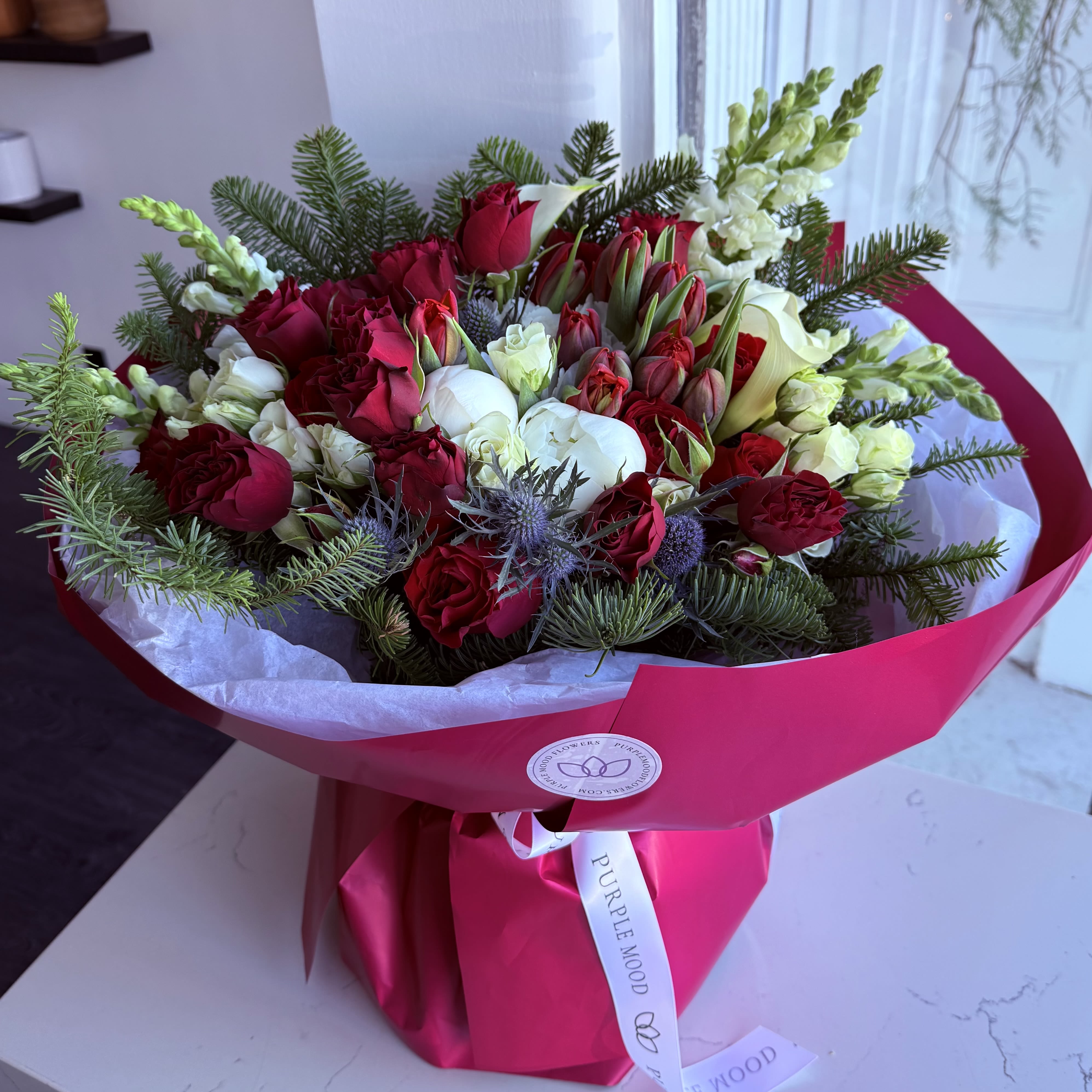 Holiday Bouquet  - Celebrate the season with our luxurious Holiday Bouquet, designed in rich festive tones of deep red, crisp white, and winter greens. This premium arrangement features a stunning mix of roses, calla lilies, tulips, snapdragons, and seasonal evergreens — creating an elegant and unforgettable holiday look.  Handcrafted with care at Purple Mood Flowers, this bouquet is perfect for gifting, holiday décor, or adding a festive touch to any home.  Vase not included