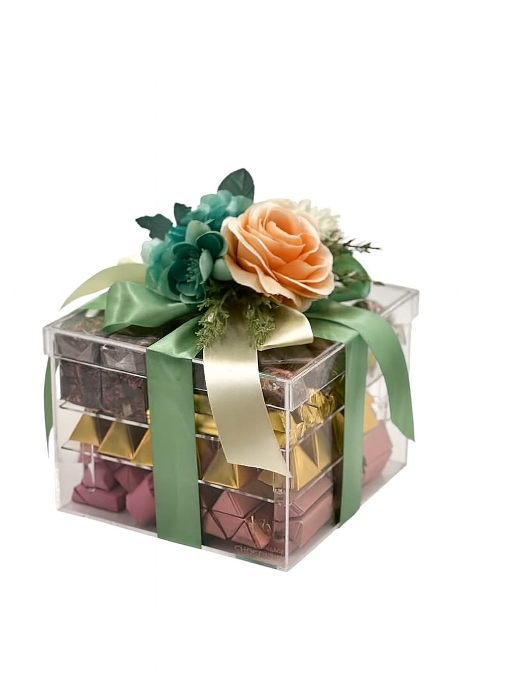 Elegance Deluxe Chocolate Box - A stunning clear acrylic gift box filled with approximately 5 pounds of premium assorted chocolates, beautifully arranged in layers of elegant foils. The box is topped with a lush floral accent in soft peach and teal tones, tied with satin ribbons for a refined, luxurious finish. A perfect gift for celebrations, corporate gifting, or anyone who loves an impressive and beautifully presented chocolate assortment.
