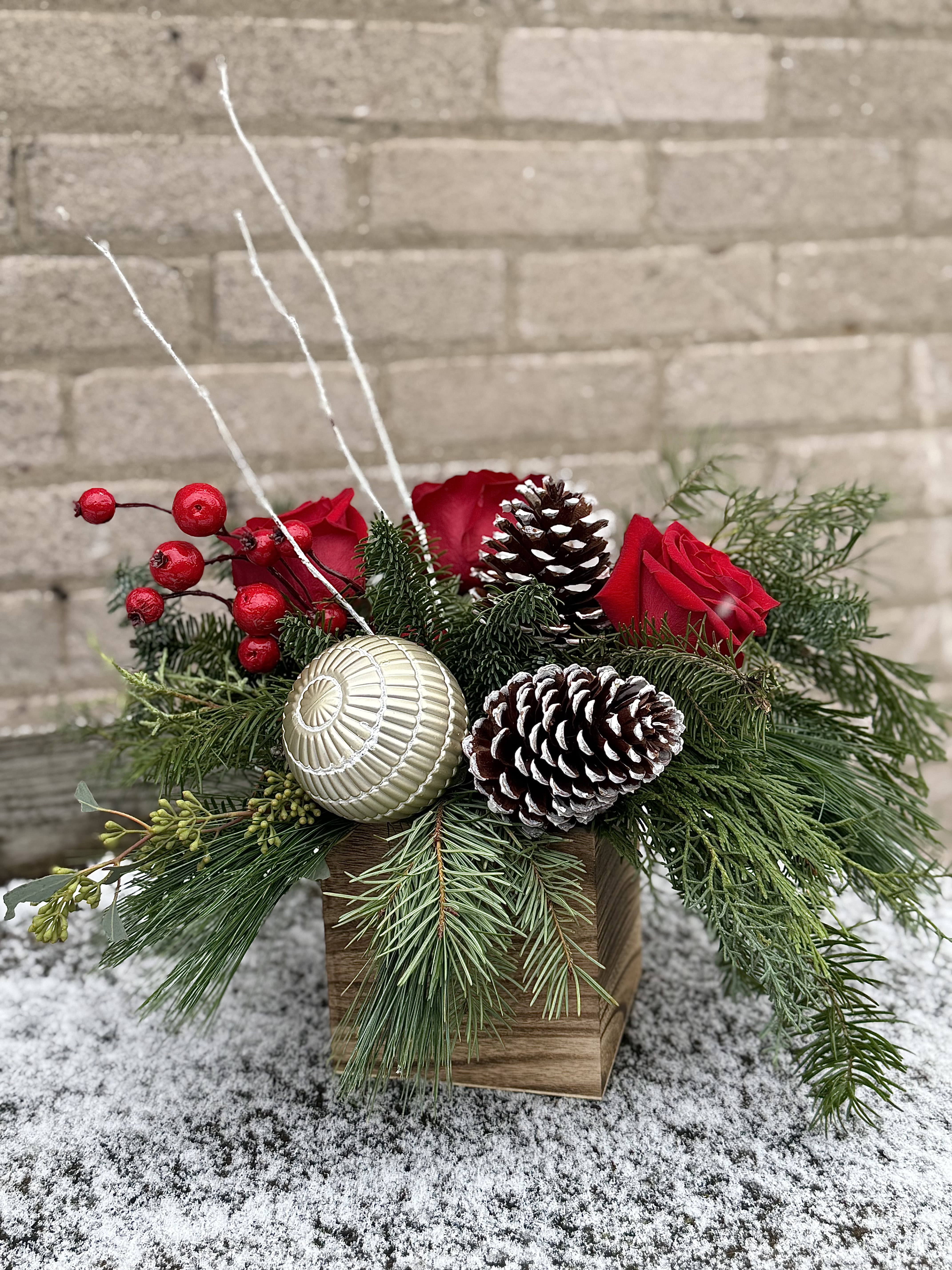 A Touch of Christmas - A lovely Christmas arrangement which can be used as a centerpiece on a medium table or a hallway table. We have added a good selection of winter greens, ornament, cones and berries and red roses. This arrangement can be ordered earlier than Christmas as it is long lasting. If you order Deluxe we will add more roses