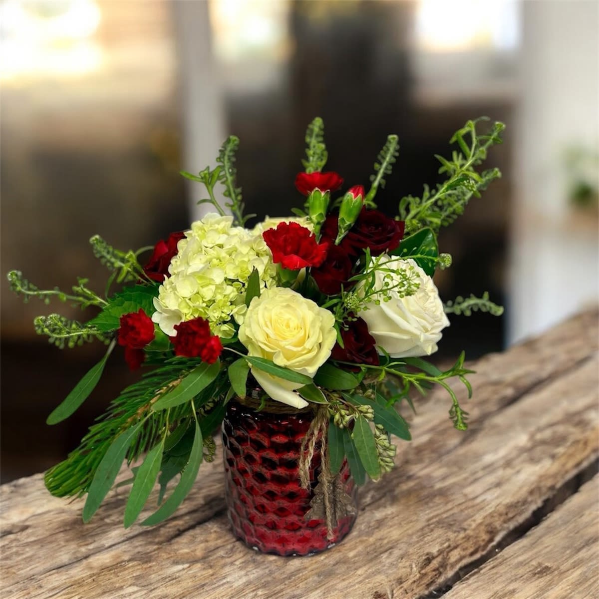 Joyful Tidings (vase vary) -  Spread holiday cheer with this stunning Christmas arrangement, featuring lush white hydrangeas, elegant roses, festive red blooms, and seasonal greenery in a beautifully textured red vase. Perfect for gifting or adding a touch of elegance to your holiday décor, this arrangement captures the spirit of the season with warmth and charm.