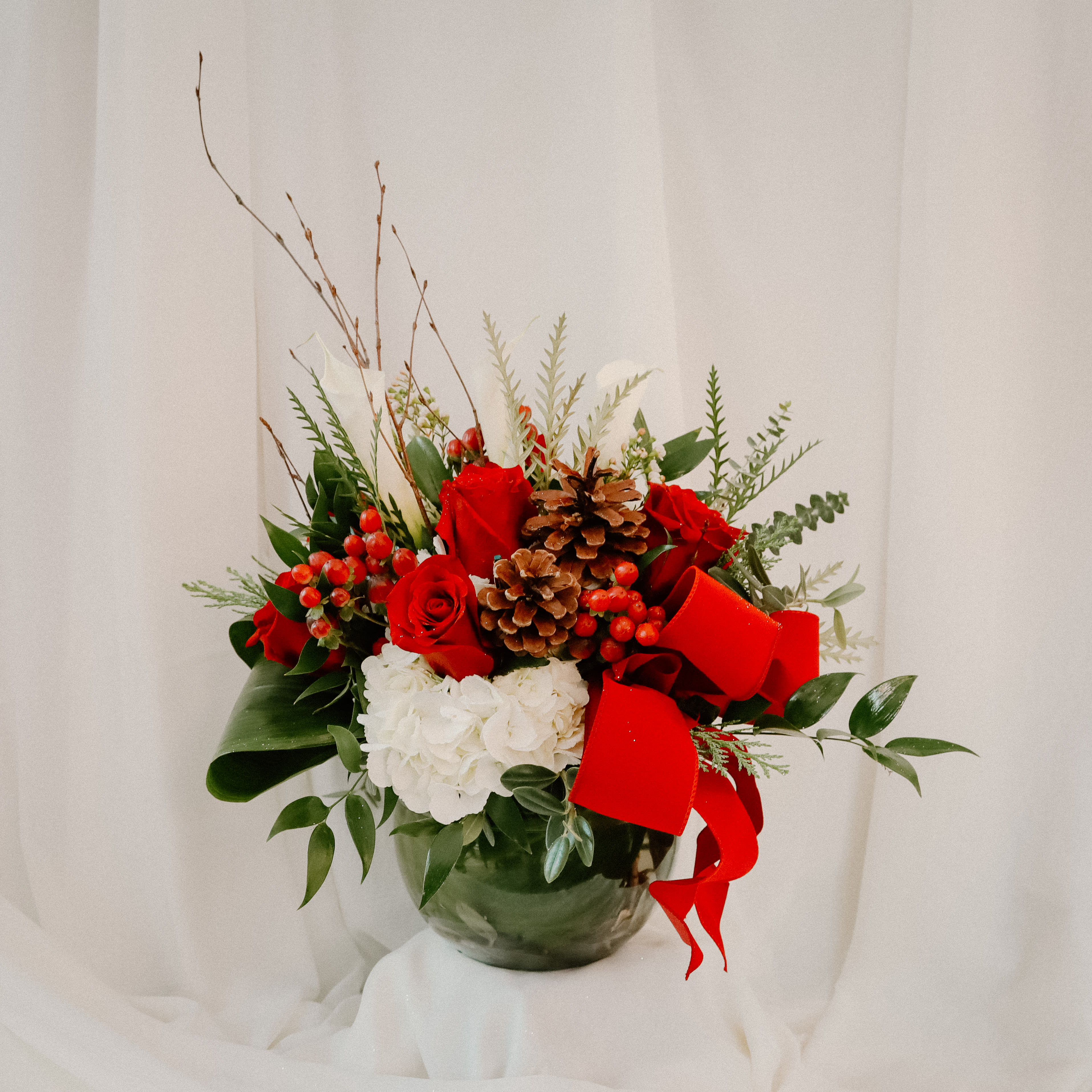 A taste of the Holiday's  - This goregous arrangement is perfect for the holiday season. It is a red and white theme and features roses, hydrangeas and a variety of greens. One of the main highlights of this arrangement are the pine cones and the beautiful red bow. 