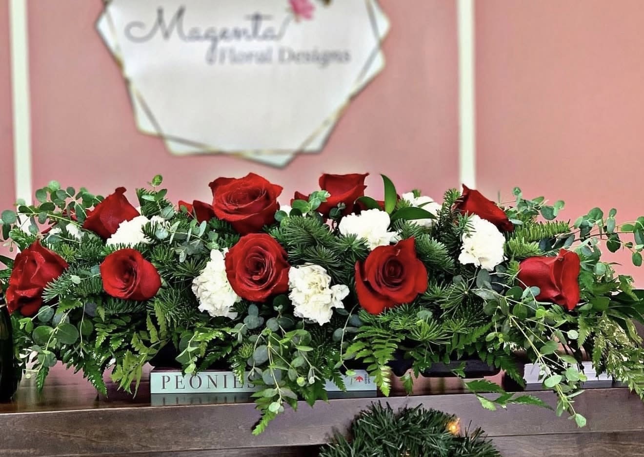 Crimson Holiday Centerpiece - Bring timeless elegance to your holiday table with our Crimson Holiday Centerpiece. Designed with lush evergreen foliage, velvety red roses, and delicate white blooms, this arrangement captures the warmth and romance of the season. Perfect for Christmas dinners, festive gatherings, or as a luxurious gift, it adds a classic and refined touch to any space. Handcrafted with care by Magenta Floral for a truly unforgettable holiday display.