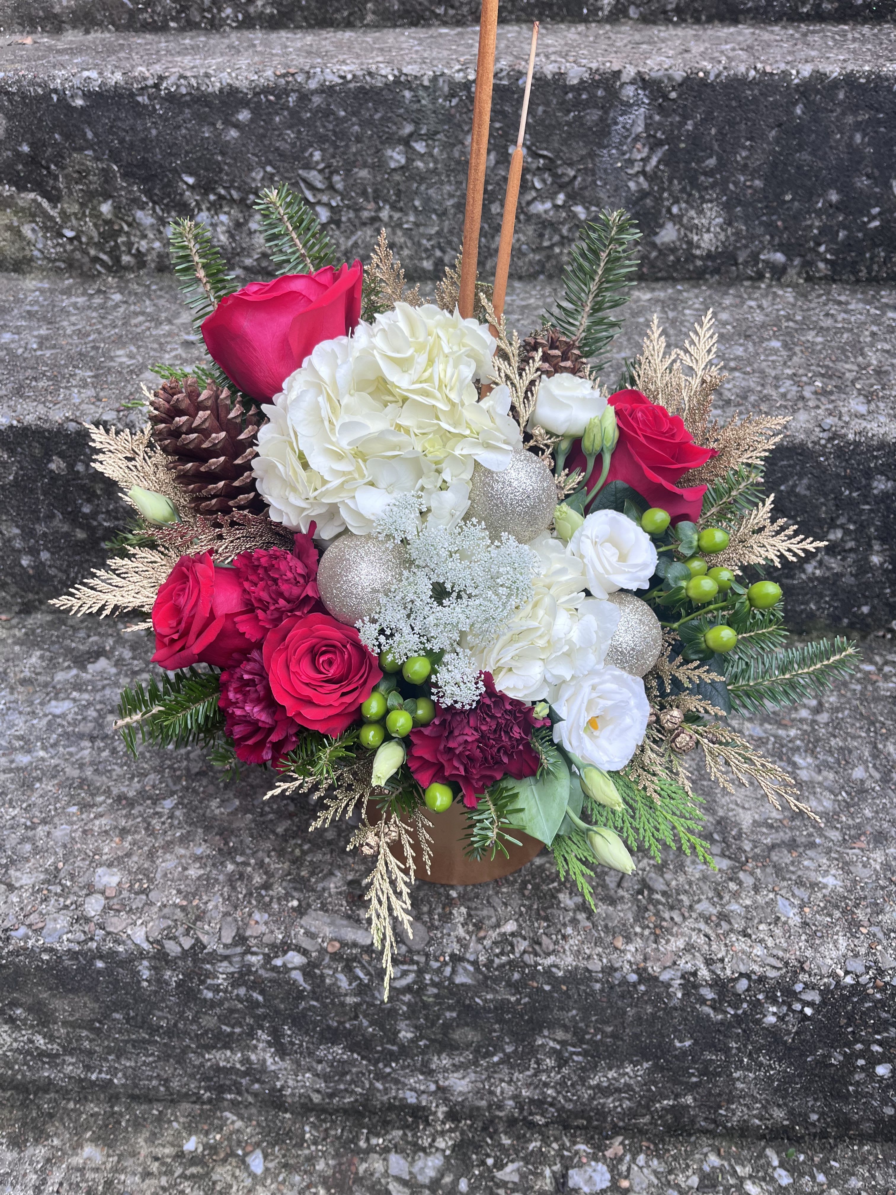 Holiday Greetings  - This arrangement has hydrangeas, roses, carnations, lisianthus , Christmas ornaments, hypericum, Queen Anne’s lace, pinecones and Christmas greens in a beautiful gold ceramic container. 