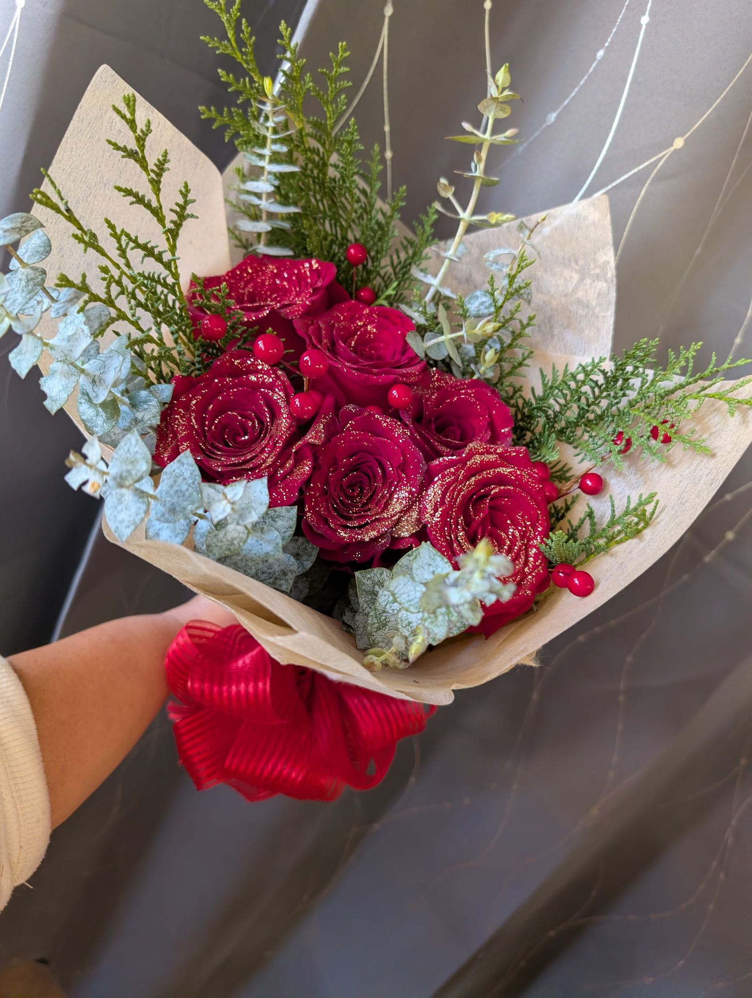 Sparkley Holiday Wrap - Deep red blooms with a sprinkle of sparkles wrapped in floral paper and finished with a bow. A perfect gift for after the big performance! 