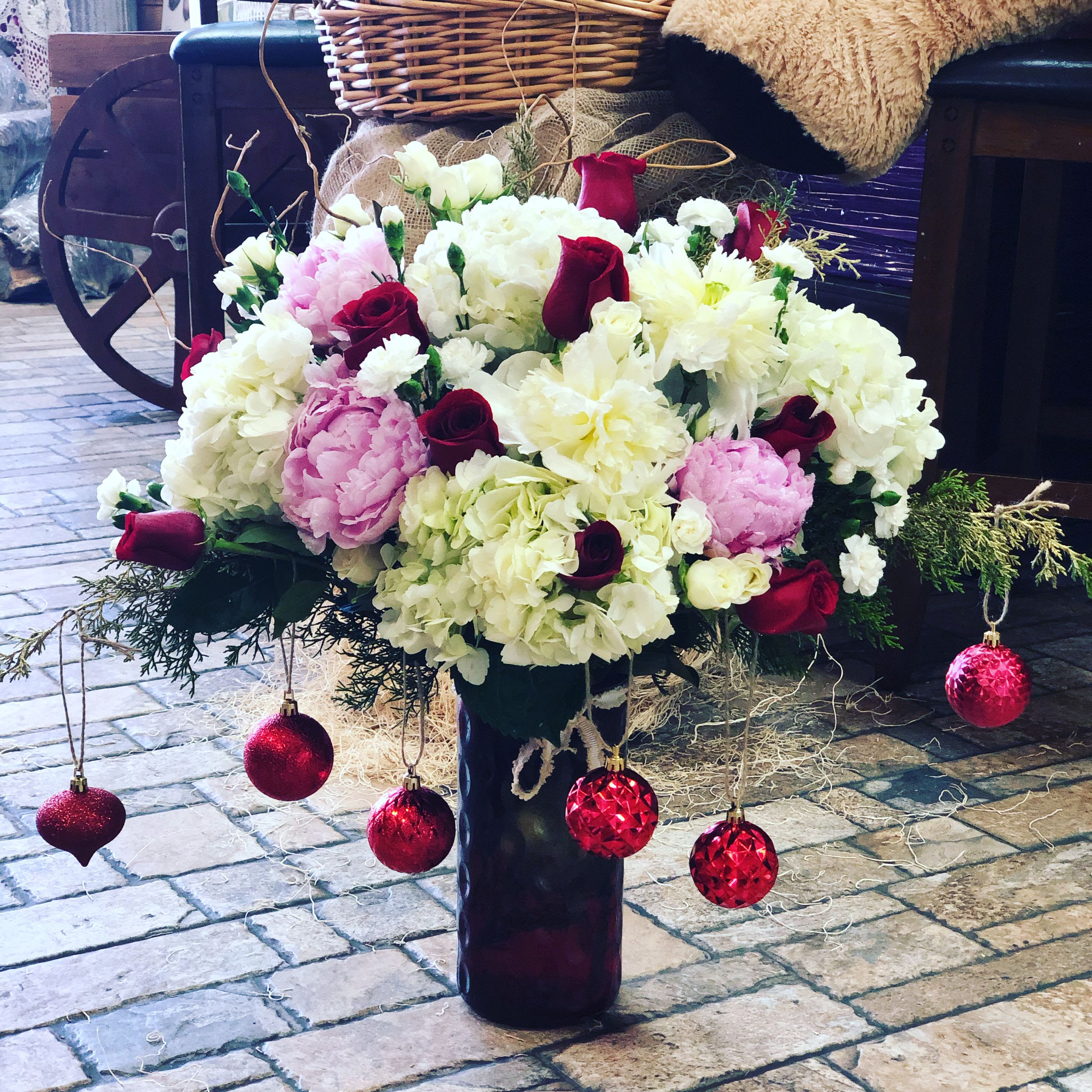 Ornamental Elegance  - Bring festive elegance into any space with this stunning holiday arrangement. This design features a lush mix of soft white, blush, and deep burgundy blooms, artfully arranged for fullness and texture. Hanging red ornaments add a playful seasonal touch, giving the bouquet a Christmas-inspired sparkle. Displayed in a sleek vase, this arrangement makes the perfect centerpiece for holiday gatherings, gifting, or adding a cheerful accent to your home décor. 