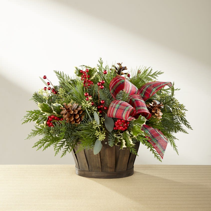 The Holiday Homecomings Basket - The Holiday Homecomings Bouquet has that rustic farmhouse look that will warm your special recipient's heart and home this holiday season! A fragrant assortment of Christmas greens are arranged with variegated holly stems and seeded eucalyptus to set the base of this holiday display. Accented with natural pinecone pics, red metallic berry pics, and a festive red and green plaid ribbon, this fresh holiday arrangement arrives in an attractive dark wooden basket to make your recipient feel as if they are truly home for the holidays once again.
