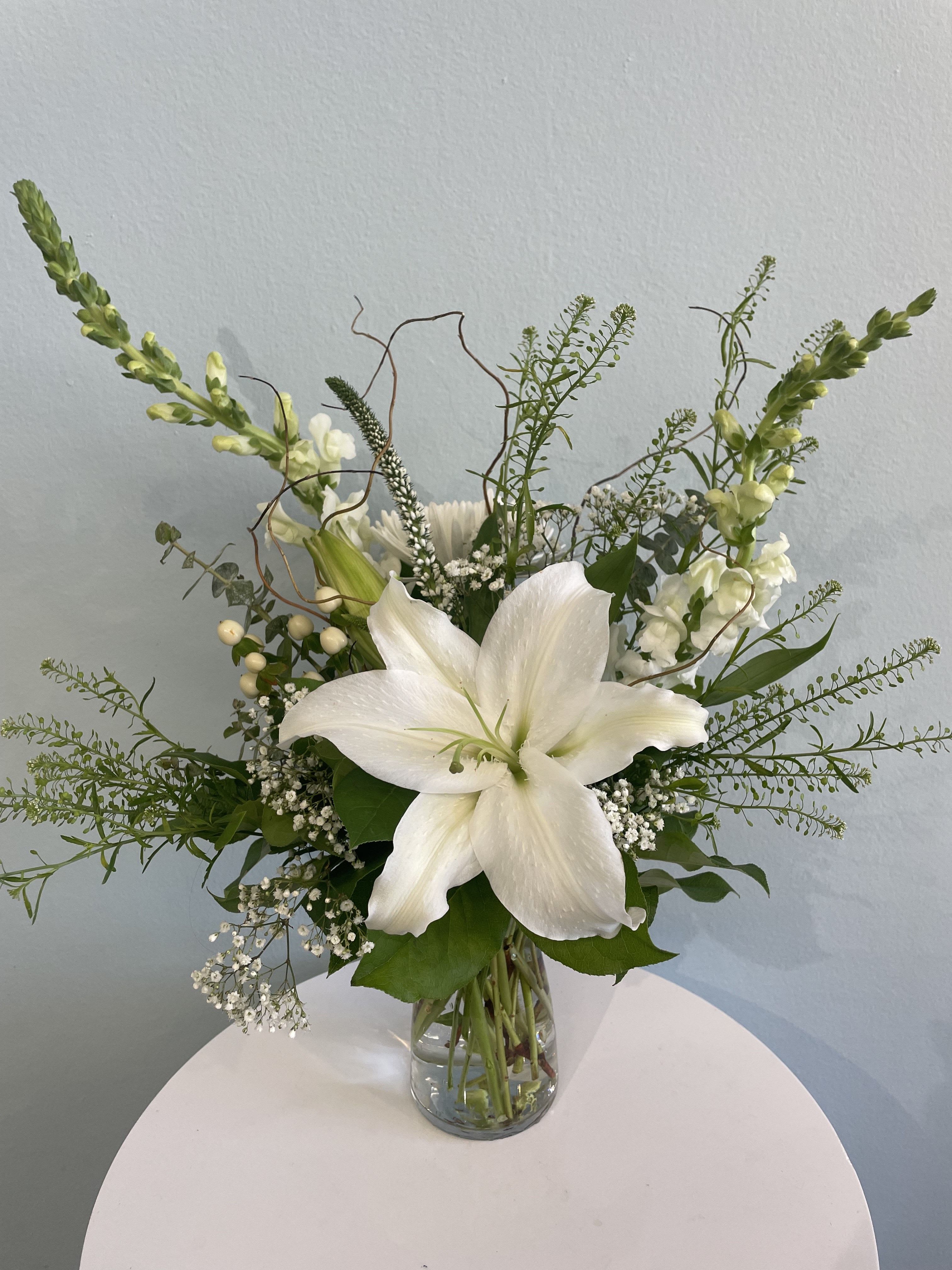 Winter Night - This small arrangement is for anyone who enjoys a classic mix of white flowers. It also makes the perfect sympathy gift. The gorgeous flowers that may be included are white lilies, snap dragons, and white fuji mums. Mixed with fragrant greenery, these white flowers are sure to pop!