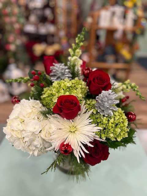 Christmas Magic (CM) - A clear glass cylinder vase filled with White and Green Hydrangea complimented with Red Roses, White Chrysanthemums, Pinecones with assorted greens make this a magical gift for that special someone. *Flowers May differ from pictured. Approximately 12 in X 12