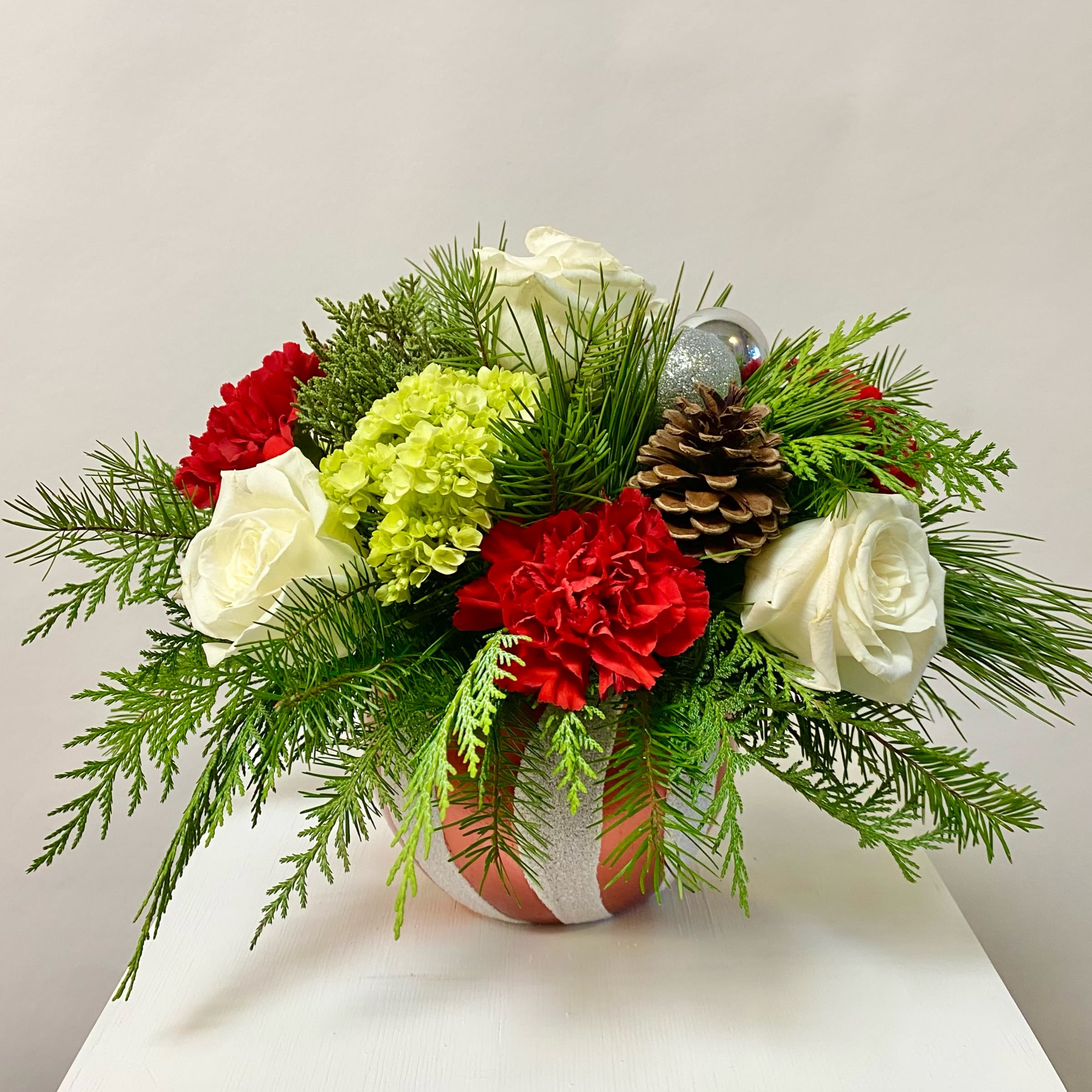 Candy Cane Ornament - This Ceramic Ornament Shaped Vase with a Functional Lid. The Arrangement Includes White Roses, Mini Green Hydrangea, Red Carnations, Pinecone and Ornament Accents. Or as Similar as Possible.