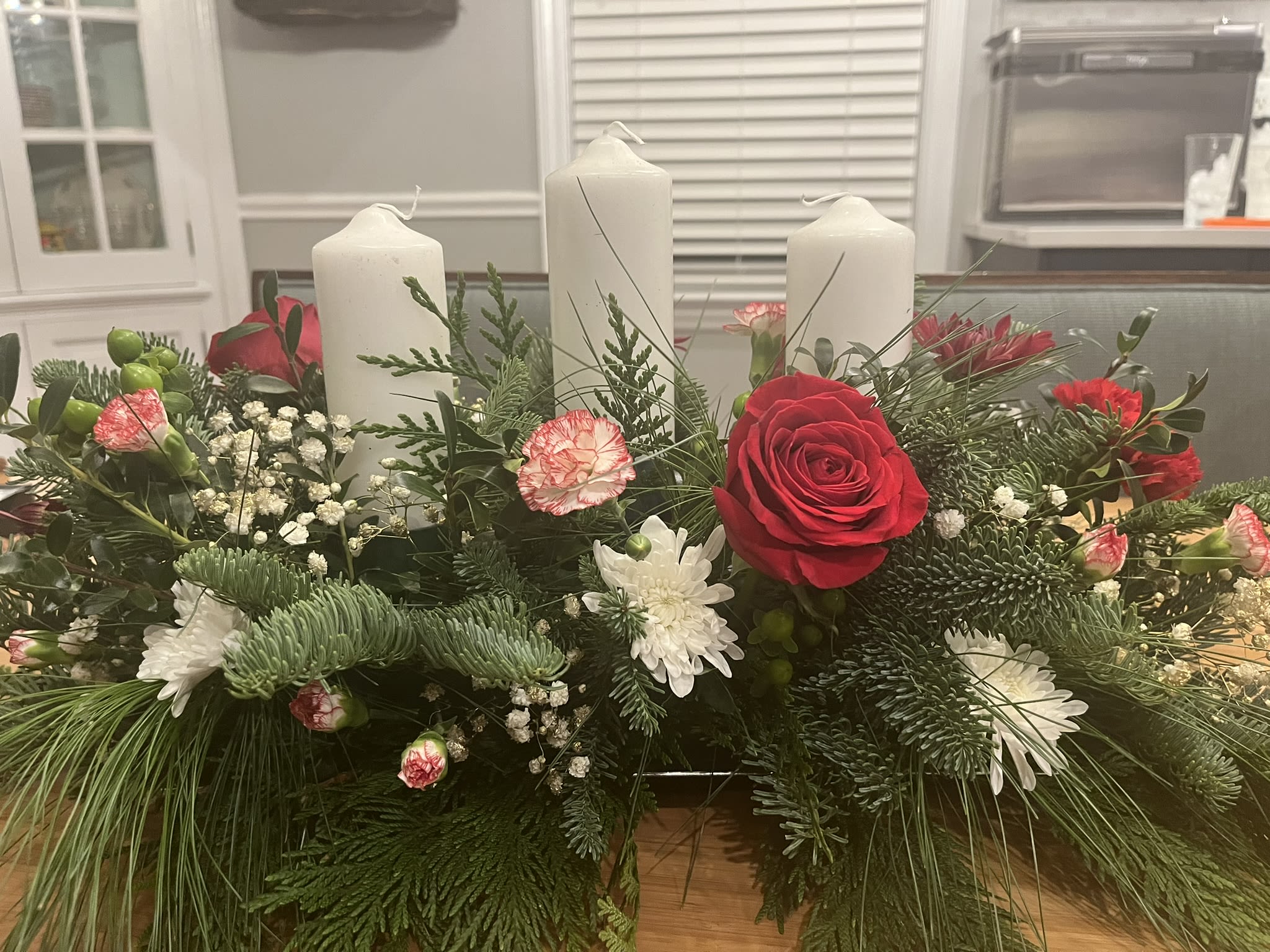 Three Candles Holiday - A holiday arrangement that sets the mood perfectly for the softness of a candlelight dinner.  Three candles (you can choose between pillar candles or taper candles) nestled in a bed of fresh fragrant greens and gorgeous red and white flowers which slight gold or silver accents.  If you have a preference, please add it to the notes! 