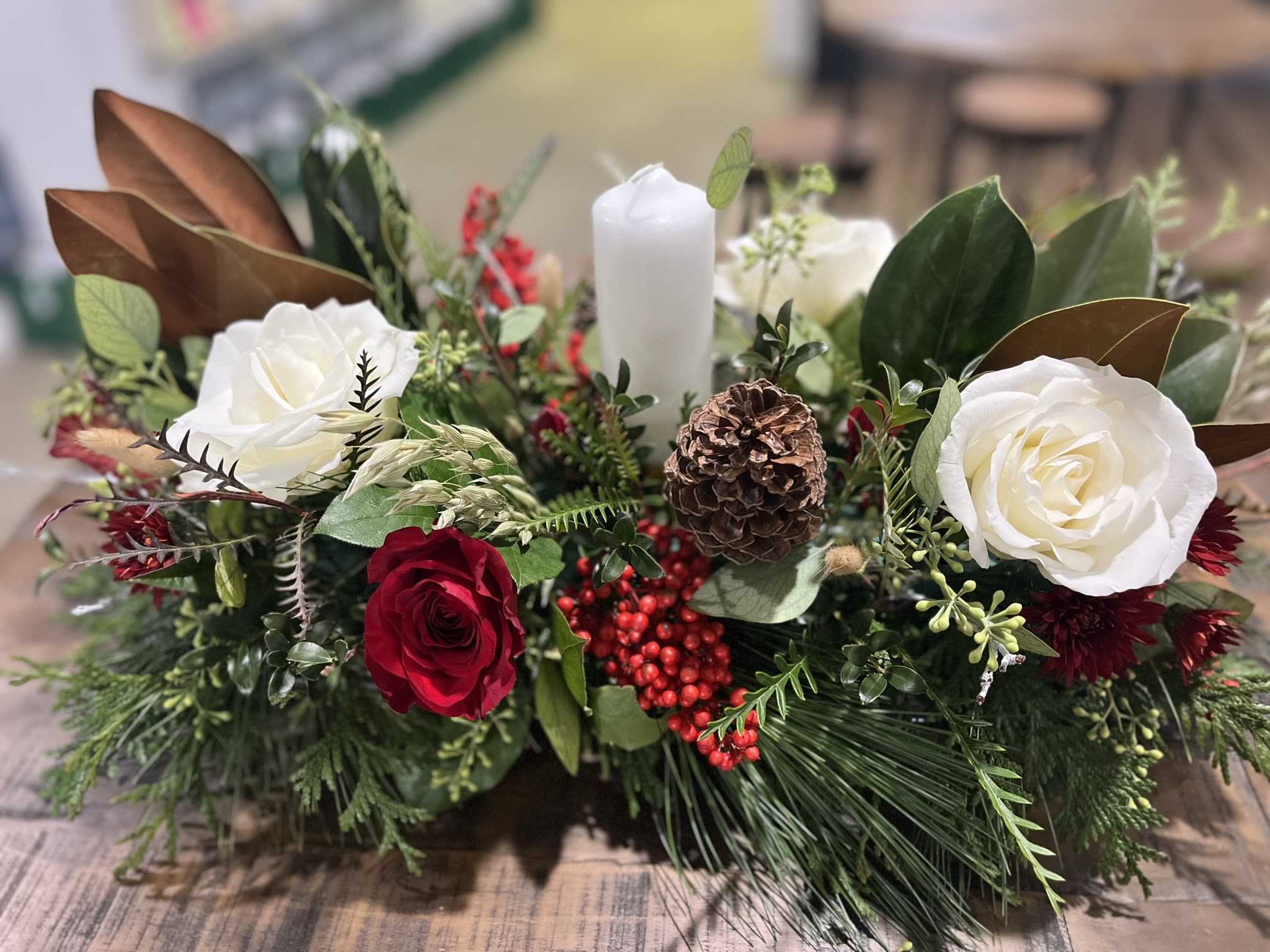 Candle in the Window - A single pillar candle in a bed of fresh fragrant evergreens dotted with red and white flowers, pinecones, berries and gold seeded eucalyptus accents.  It's classic and elegant for any holiday event.