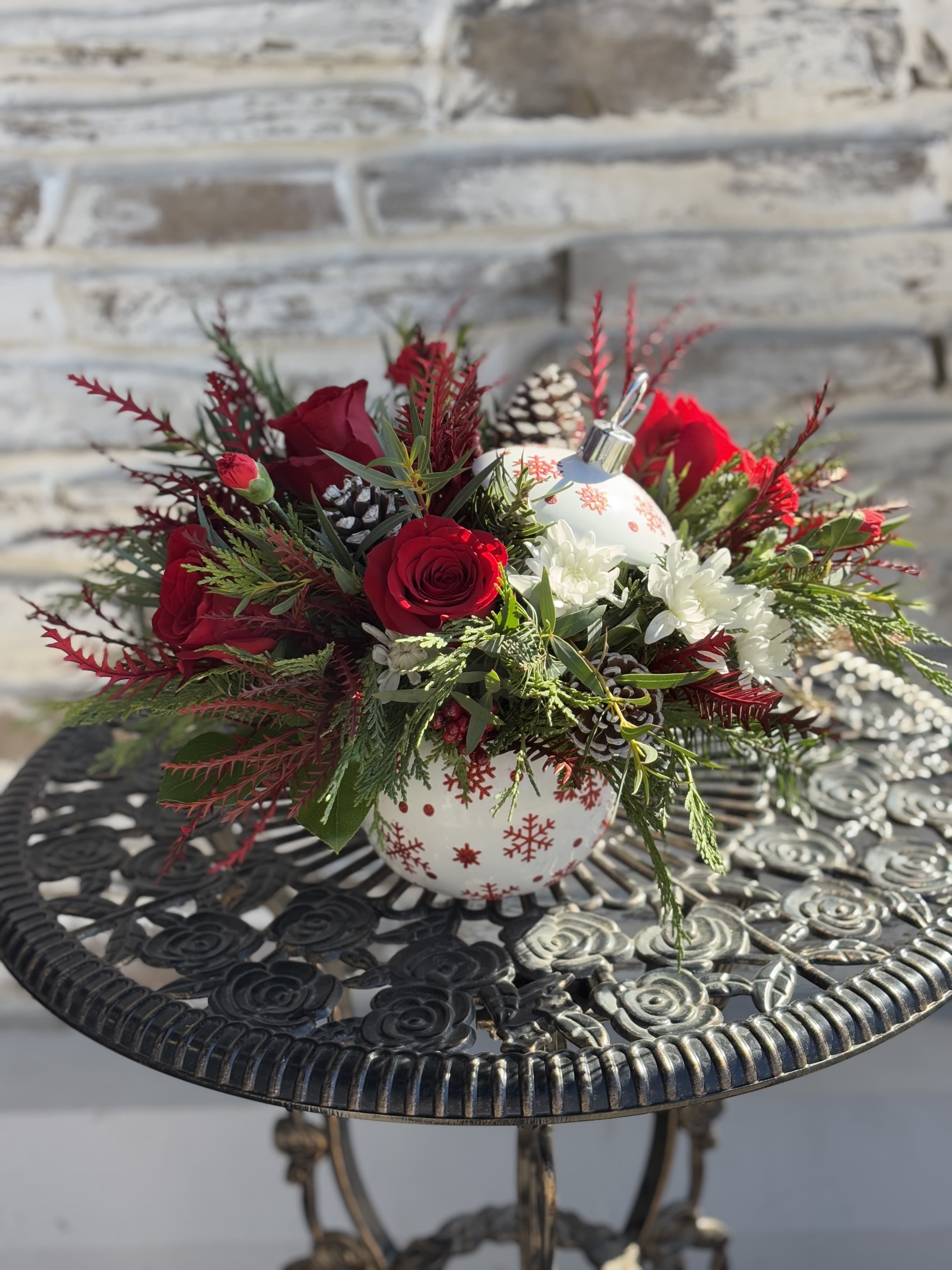White Sparkle Ornament - Brighten your Christmas with a vibrant red roses and winter greens, beautifully arranged in a hand-painted, ceramic ornament jar with sparkling stars. It's perfect for holding wrapped candies and holiday treats afterward! This arrangement features red roses, miniature red carnations, white spray chrysanthemums, white pinecones and assorted greenery. 