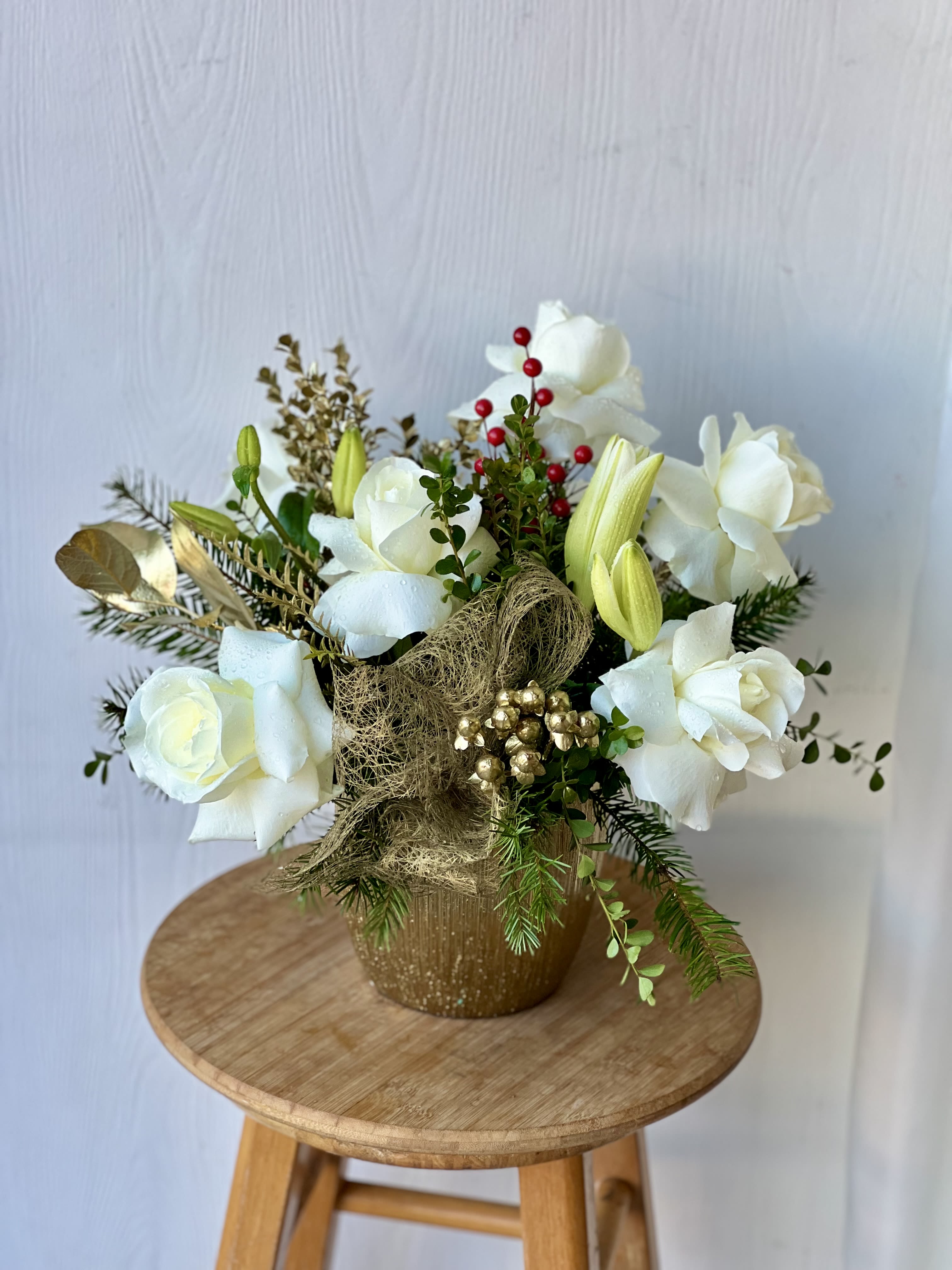 Golden Winter - Bring a touch of luxury to your holiday décor with our Golden arrangement. Designed in a premium white ceramic vase, this medium-sized Christmas centerpiece features lush white roses, elegant white lilies, and festive gold leaves accented with shimmering gold ribbon. The timeless white-and-gold palette adds a sophisticated sparkle to any room, making it perfect for holiday dinners, gifting, or elevating your seasonal home décor.  Handcrafted with fresh, high-quality blooms, this arrangement offers a modern yet classic Christmas look—ideal for those who love clean, elegant styling with a hint of festive glamour.  Perfect for: holiday centerpieces, corporate gifts, Christmas parties, home décor, and winter celebrations.