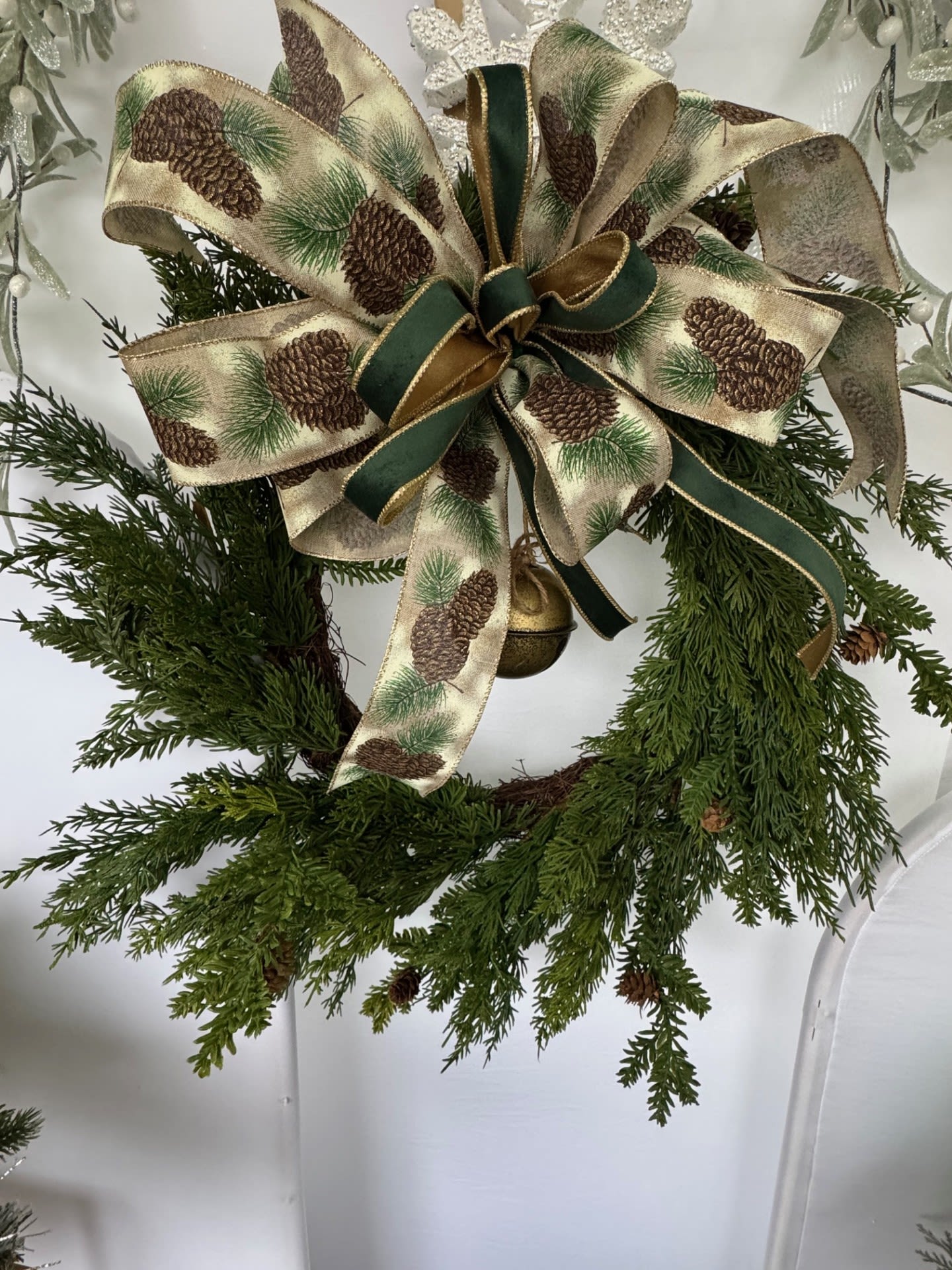 Evergreen Silk Christmas Wreath - Green Christmas Silk Wreath with Pine Cones &amp; Ribbons  Bring timeless holiday elegance to your home with our Green Christmas Silk Wreath, handcrafted to capture the warmth and magic of the season. Lush, high-quality silk greenery creates a full, vibrant base, accented with natural pine cones for a touch of rustic charm. Soft golden ribbon weaves through the foliage, adding a subtle shimmer that catches the light and elevates any space with festive sophistication.  Perfect for doors, mantels, entryways, or as a statement wall piece, this wreath blends traditional holiday style with modern luxury. Durable and beautifully crafted, it’s designed to stay stunning year after year—no maintenance required.  Features:  Premium silk greenery for a realistic, lush look Natural pine cones for added texture and warmth Elegant gold ribbon for a festive glow Ideal for indoor or covered outdoor display A beautiful seasonal accent for homes, offices, or gift-giving  Celebrate the season with a wreath that welcomes guests with classic Christmas charm and effortless elegance.