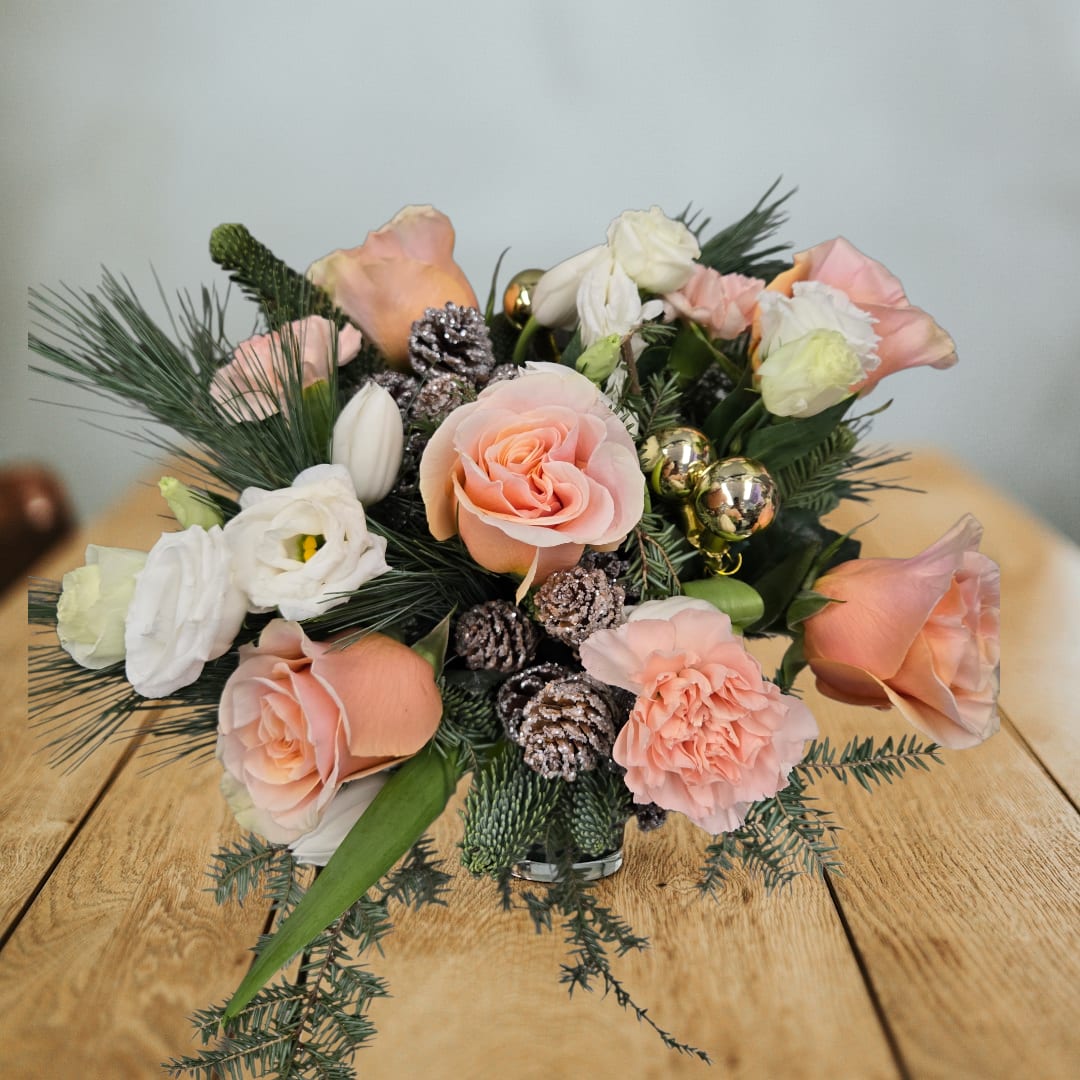 Peach &amp; Pine Holiday Hearth  - Peach &amp; Pine Holiday Hearth      brighten your holiday decor with the warm hues of a warm indoor winter cozy fire. This playful arrangement showcases peach roses in peach carnations, white tulips, white lisanthus , paired with lush greens, rustic pinecones, . Compact yet striking, it’s a delightful way to add festive cheer to your home or office.   Measuring 8” wide and 8” tall, winter warmth is perfect for small spaces or gifting. Its unique color palette and elegant accents make it a standout piece for the holiday season.   The arrangement is 8″ wide x 8″ tall. 