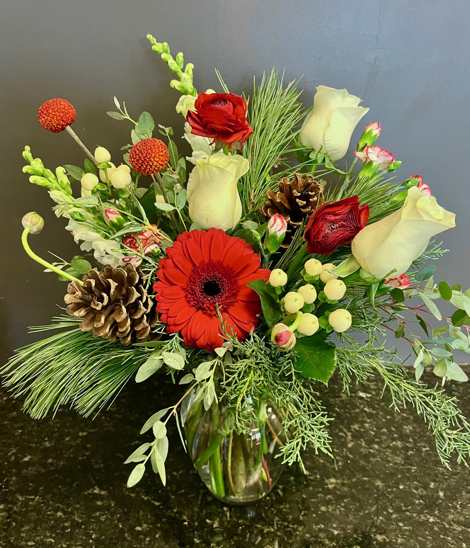 Winter Cottage - Red Gerber, White roses and red ranunculus are accented with peppermint pixie carnations,  berries and greens in a glass vase