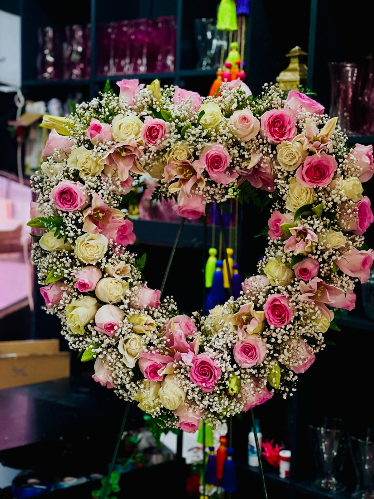 Eternal Grace Wreath - This stunning heart-shaped floral wreath is a symbol of love and remembrance. Crafted with soft pink and cream roses, complemented by delicate lilies, lush greenery, and ethereal baby's breath, this design exudes elegance and serenity. Perfect for memorial services, weddings, or as a heartfelt decorative piece, the &quot;Eternal Grace Wreath&quot; radiates timeless beauty and tenderness, making it a meaningful expression of emotions.  