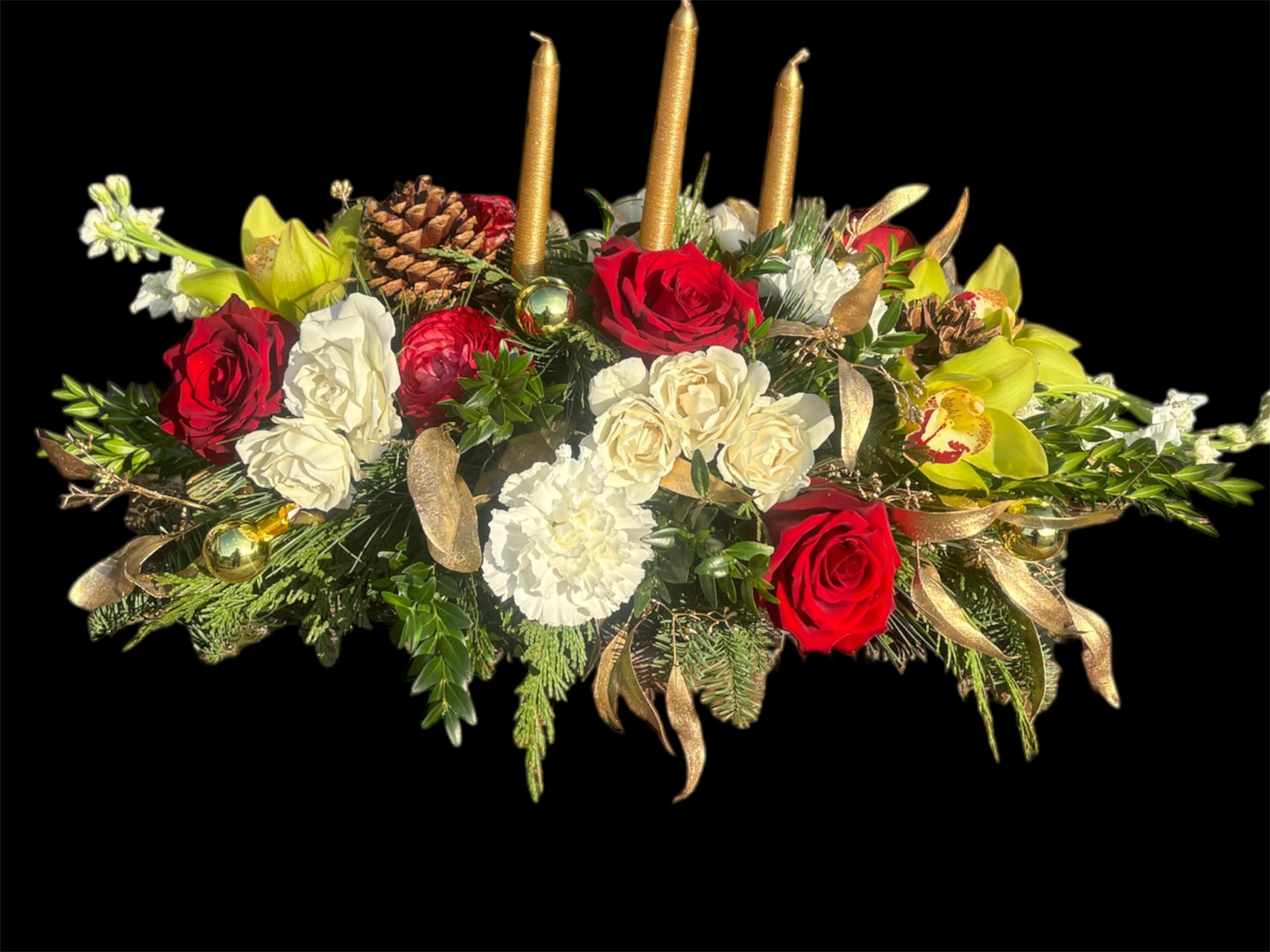 Encanto Dorado - A stunning mix of red roses, delicate white spray roses, soft white carnations, vibrant red ranunculus, fragrant white stock, and exotic green cymbidium orchids. Accented with natural pinecones, shimmering gold embellishments, and surrounded by lush winter greenery, the design is completed with three gold candles that add a warm, festive glow. Perfect for bringing elegance and holiday cheer to any celebration.