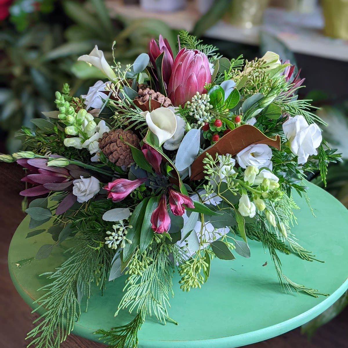 Warm Winter Wishes  - Send some warmth this season with a beautiful arrangement featuring exotic proteas. This is designed with seasonal greens, reds and whites. 