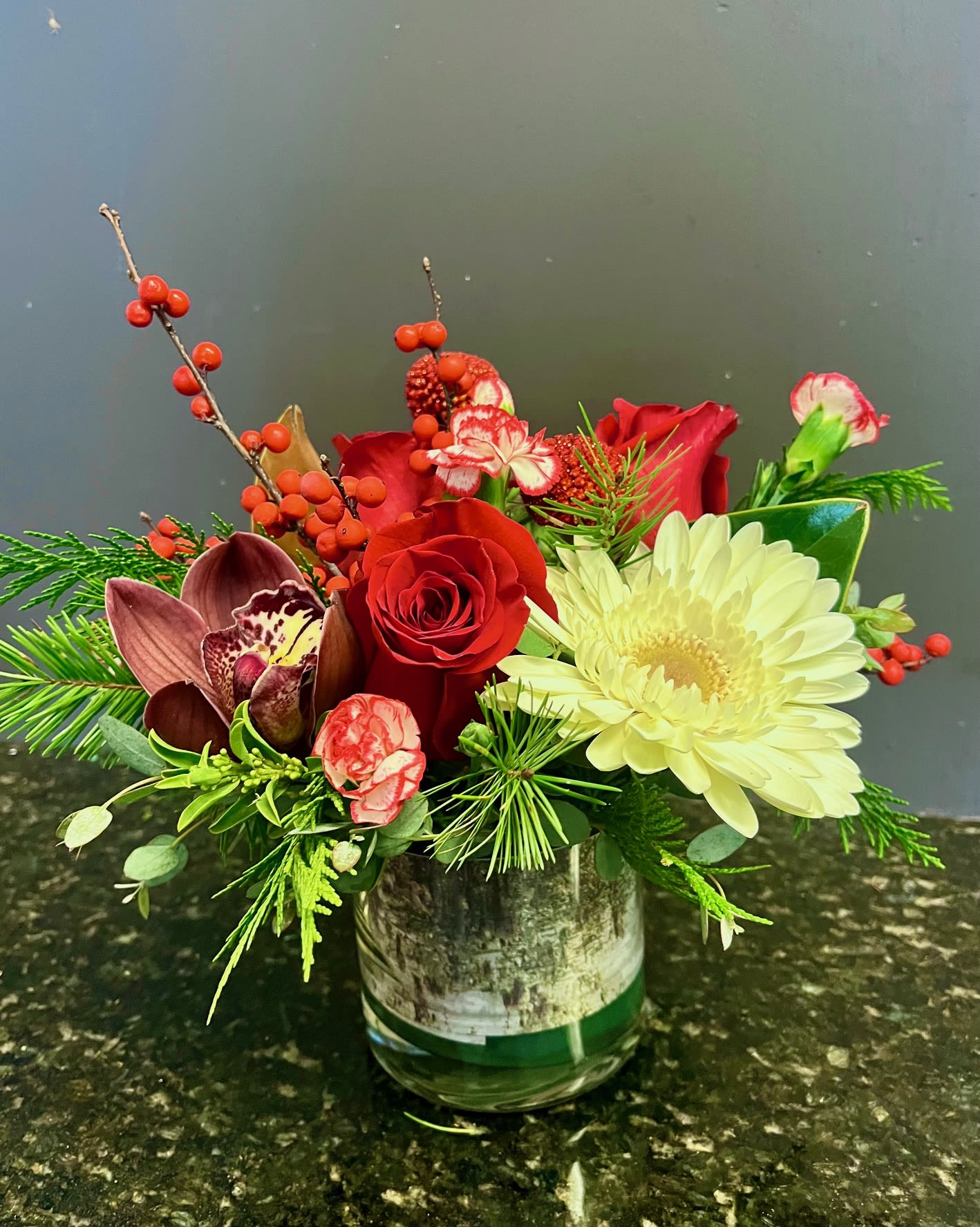 Santa's Gift - Enjoy the holiday season with this elegant table piece which includes winter berries, gerber daisy, red roses, peppermint carnations and a cymbidium orchid bloom. 
