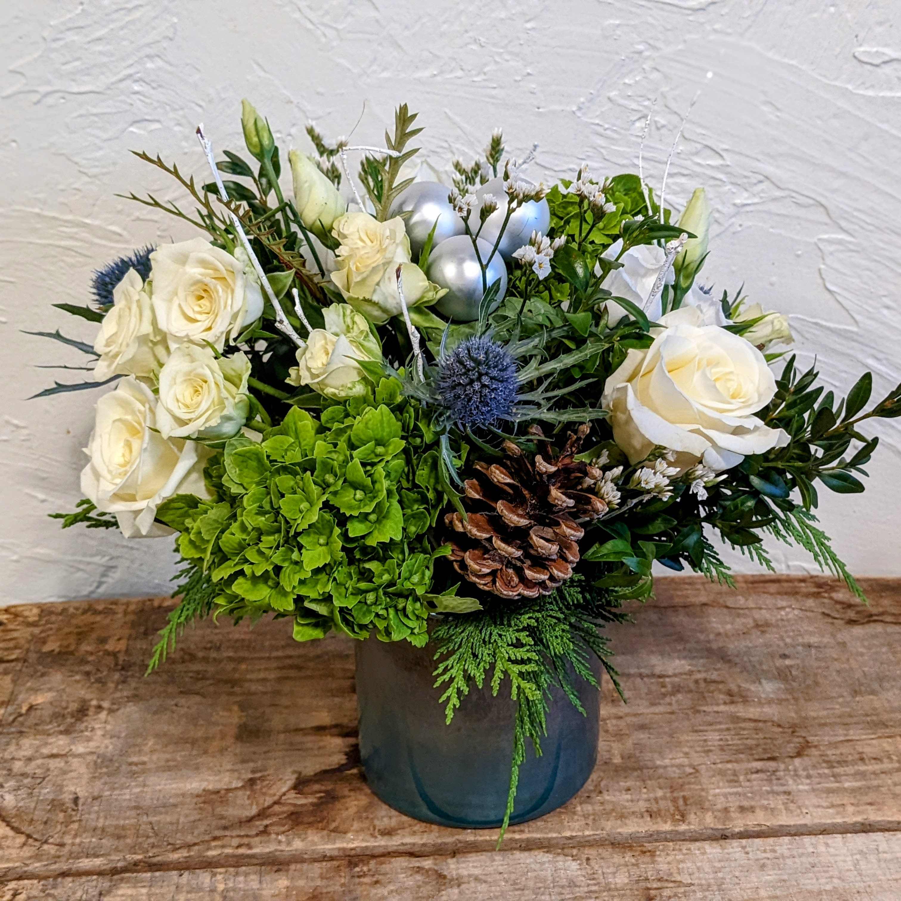 Winter's Frost - Send a frosty winter arrangement perfect for any occasion. This arrangement is features a variety of flowers including roses, lisianthus, green hydrangea, eryngium, and festive seasonal decor.   