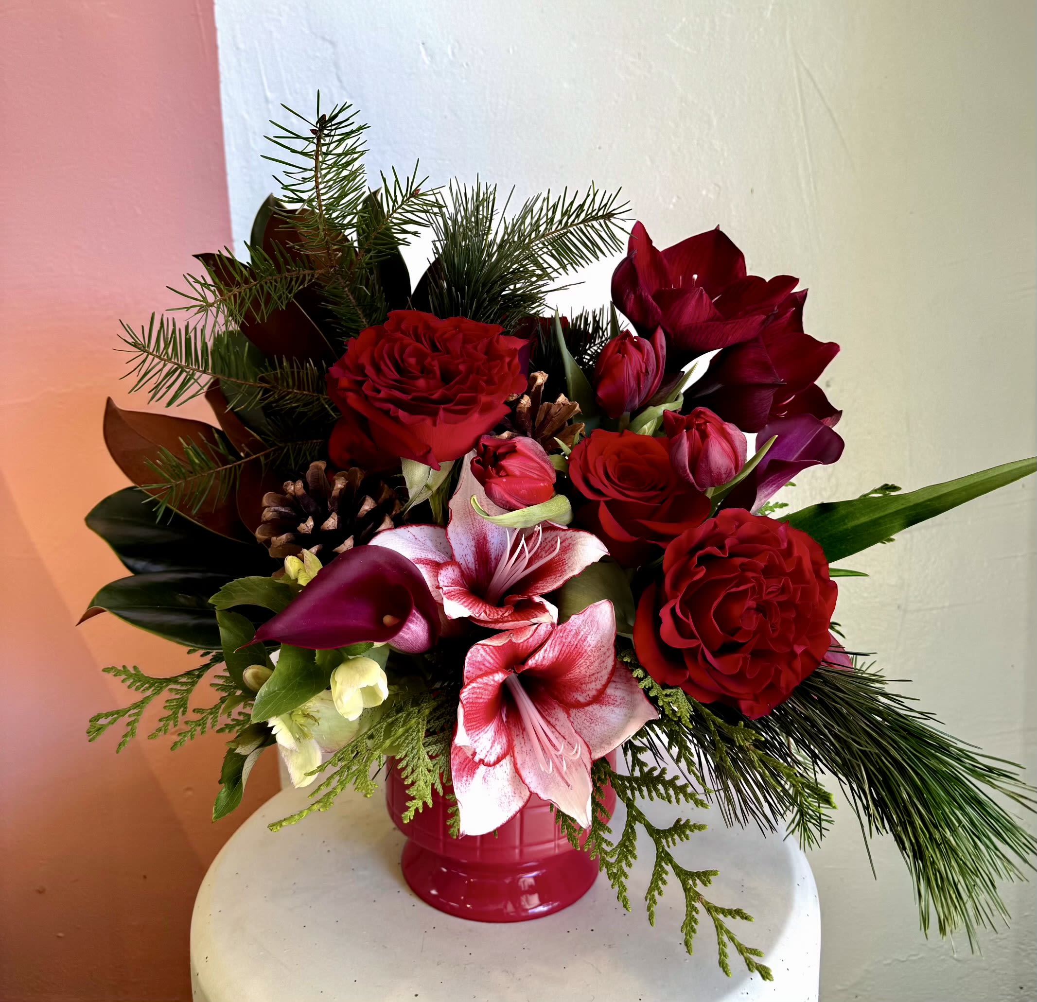 Noel - Created in a red compote vase,  with red amaryllis, red roses and holiday greenery. 