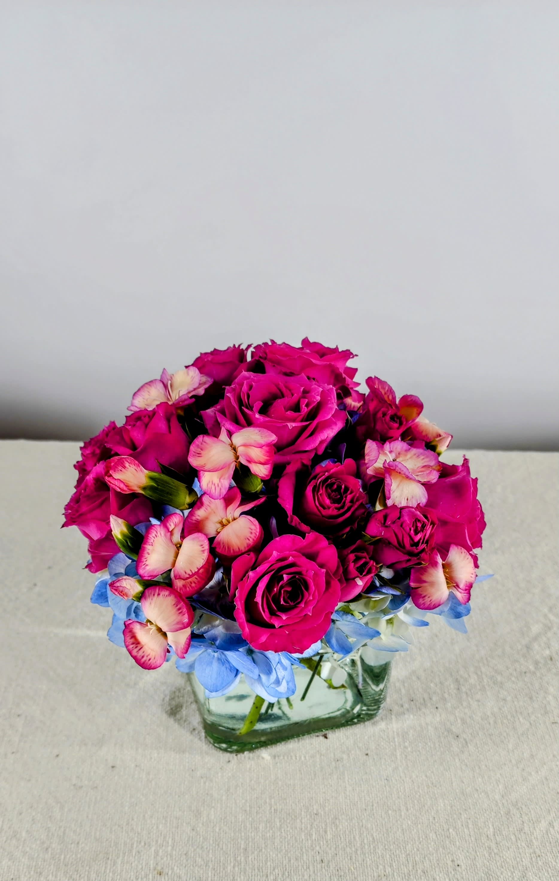 Square Me Up - available in multiple colors. Please call for availability. - Blue hydrangeas, spray roses, miniature carnations &amp; dianthus fill this cube vase.  A fun flower arrangement to brighten your special ones day.